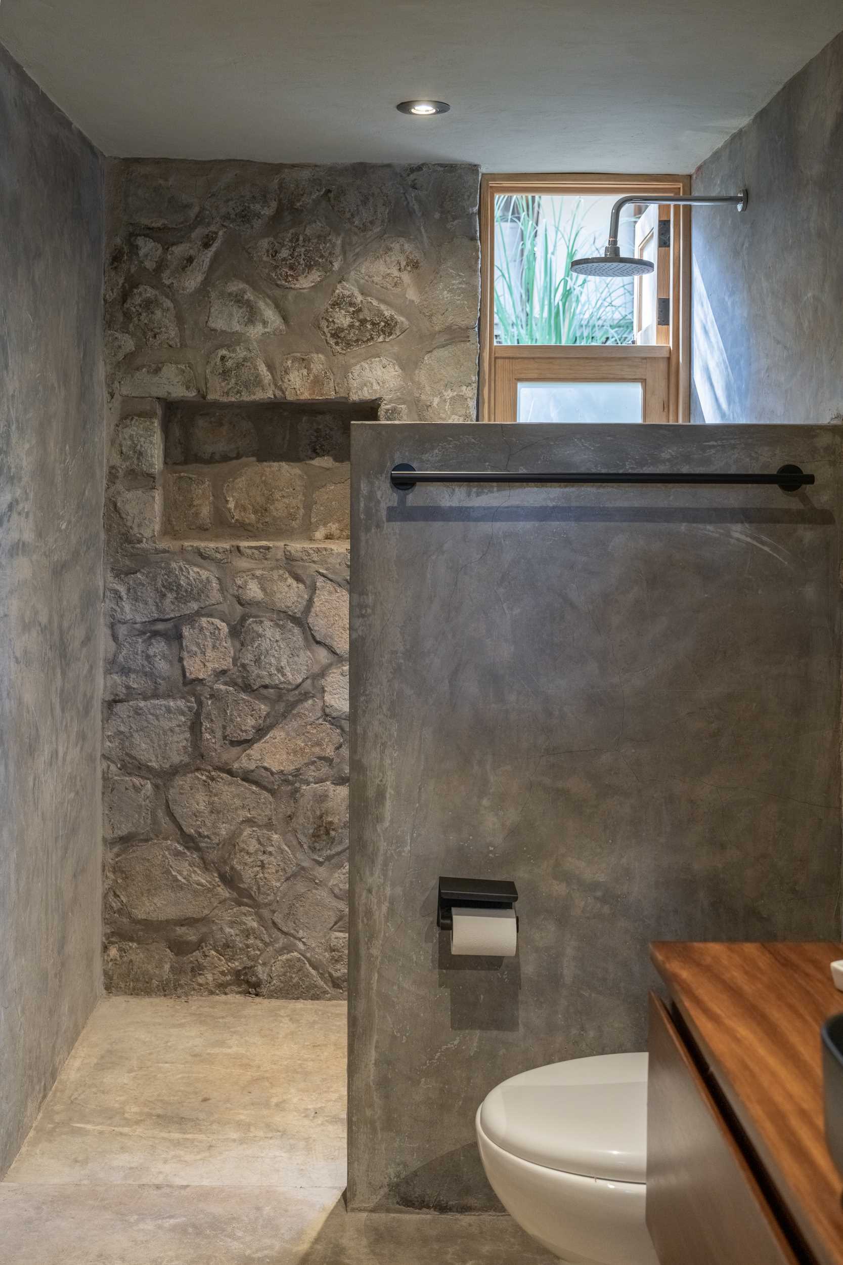 A modern stone and wood bathroom that includes a partial wall that separates the shower from the rest of the space.