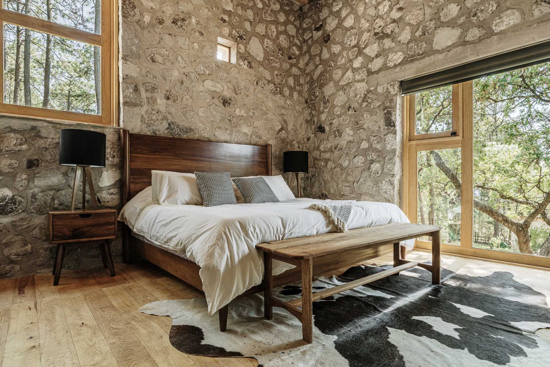 A modern stone and wood bedroom with treetop views.