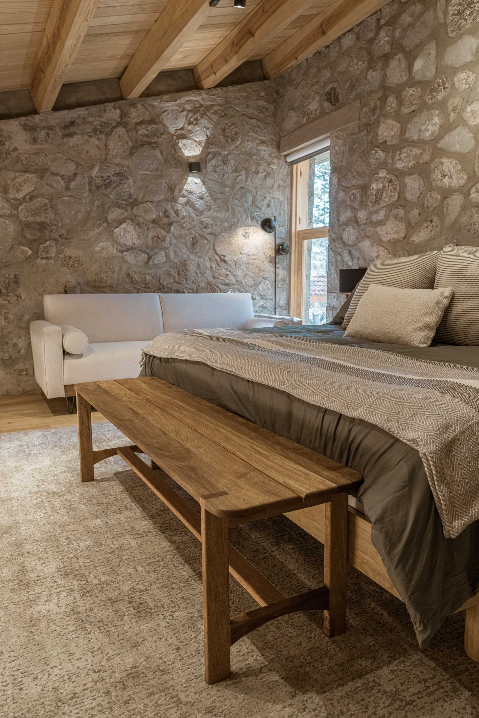 A modern loft bedroom with stone walls, wood floors, and cozy furniture.