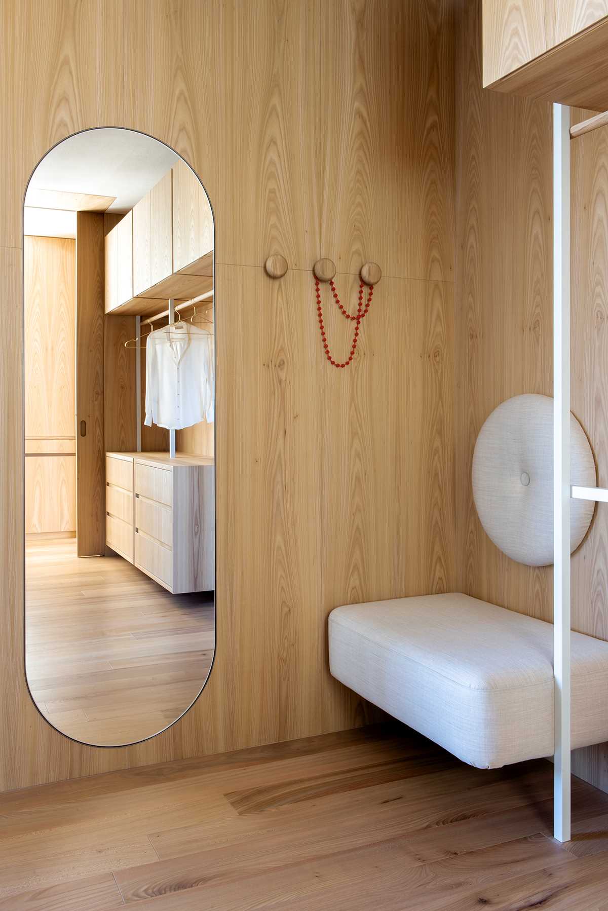 A walk-in closet lined in wood has a pill-shaped mirror that complements other arched accents found around the home.