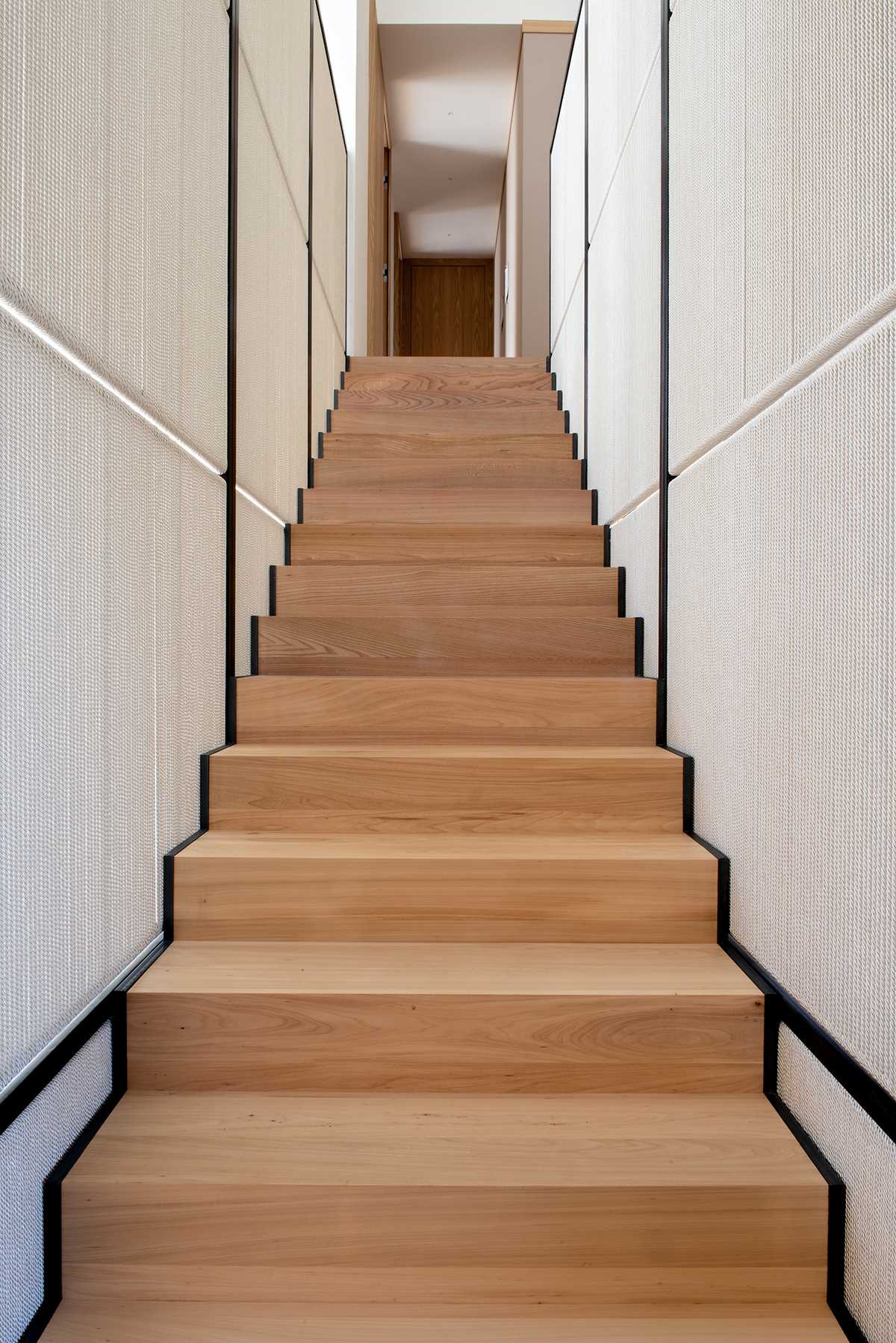 Modern wood stairs lead to a hallway with a wall of wood cabinets.