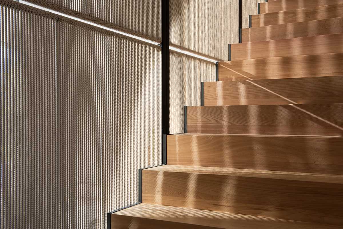 Modern wood stairs lead to a hallway with a wall of wood cabinets.