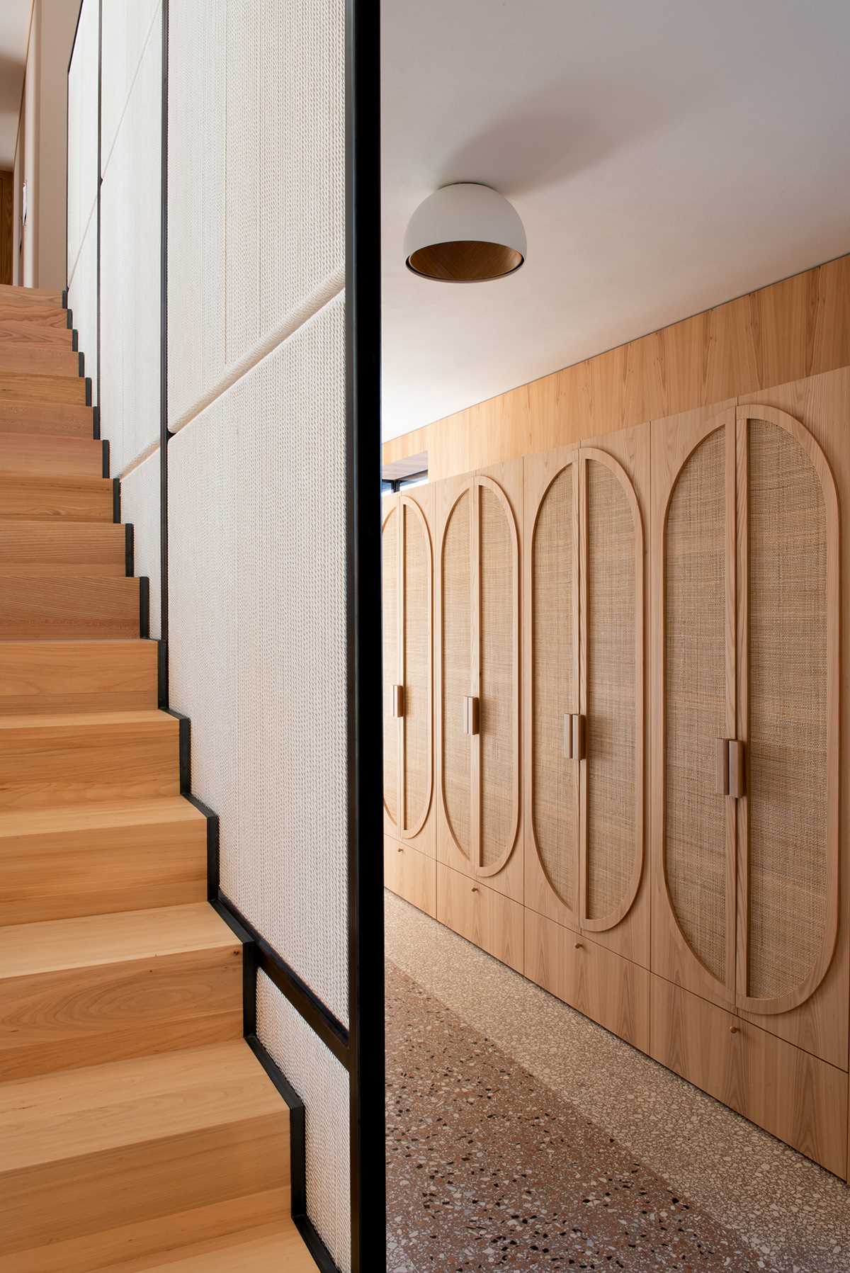 Modern wood stairs lead to a hallway with a wall of wood cabinets.