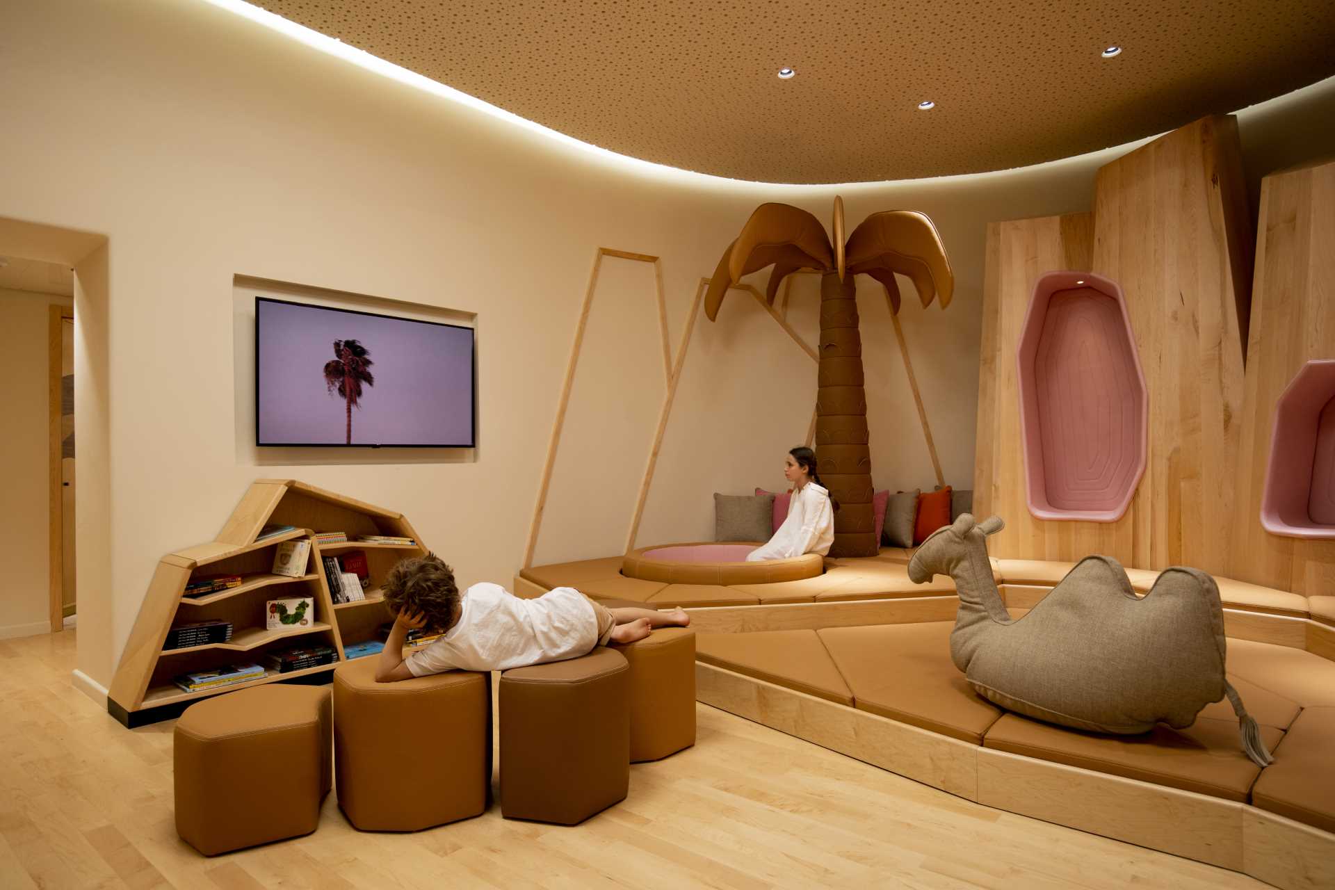 A modern kids playroom inspired by the desert, with sand dunes, sculptural desert mountains, camels, and palm trees.