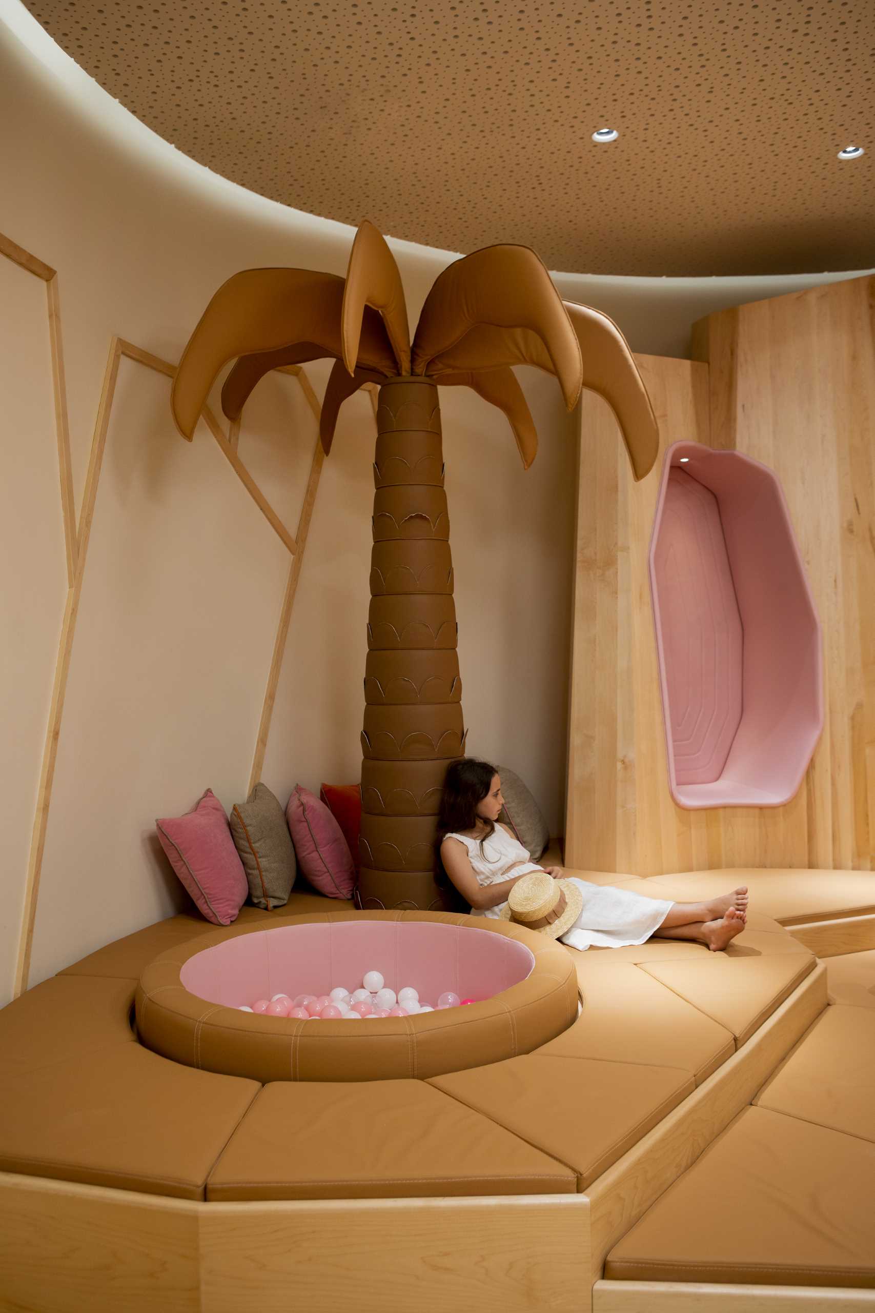 A modern kids playroom inspired by the desert, with sand dunes, sculptural desert mountains, camels, and palm trees.