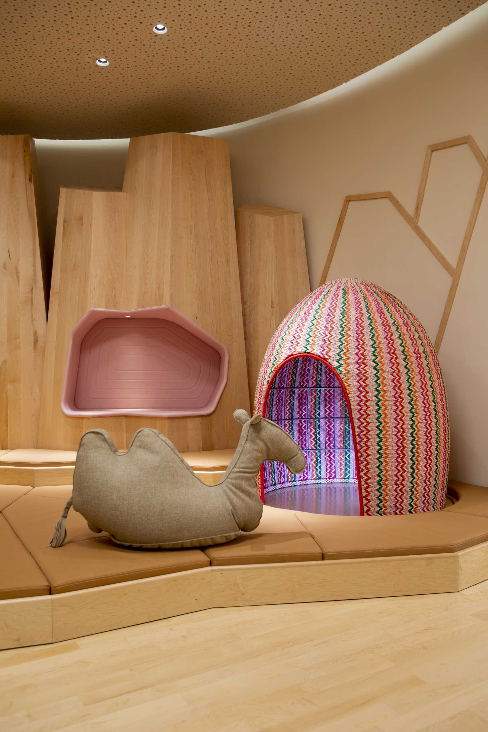 A modern kids playroom inspired by the desert, with sand dunes, sculptural desert mountains, camels, and palm trees.