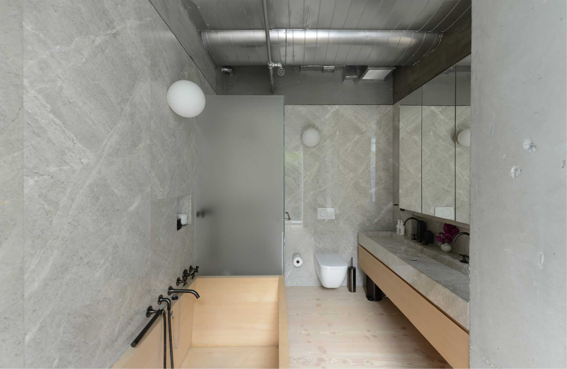 A modern bathroom with grey stone walls and a wood bathtub.