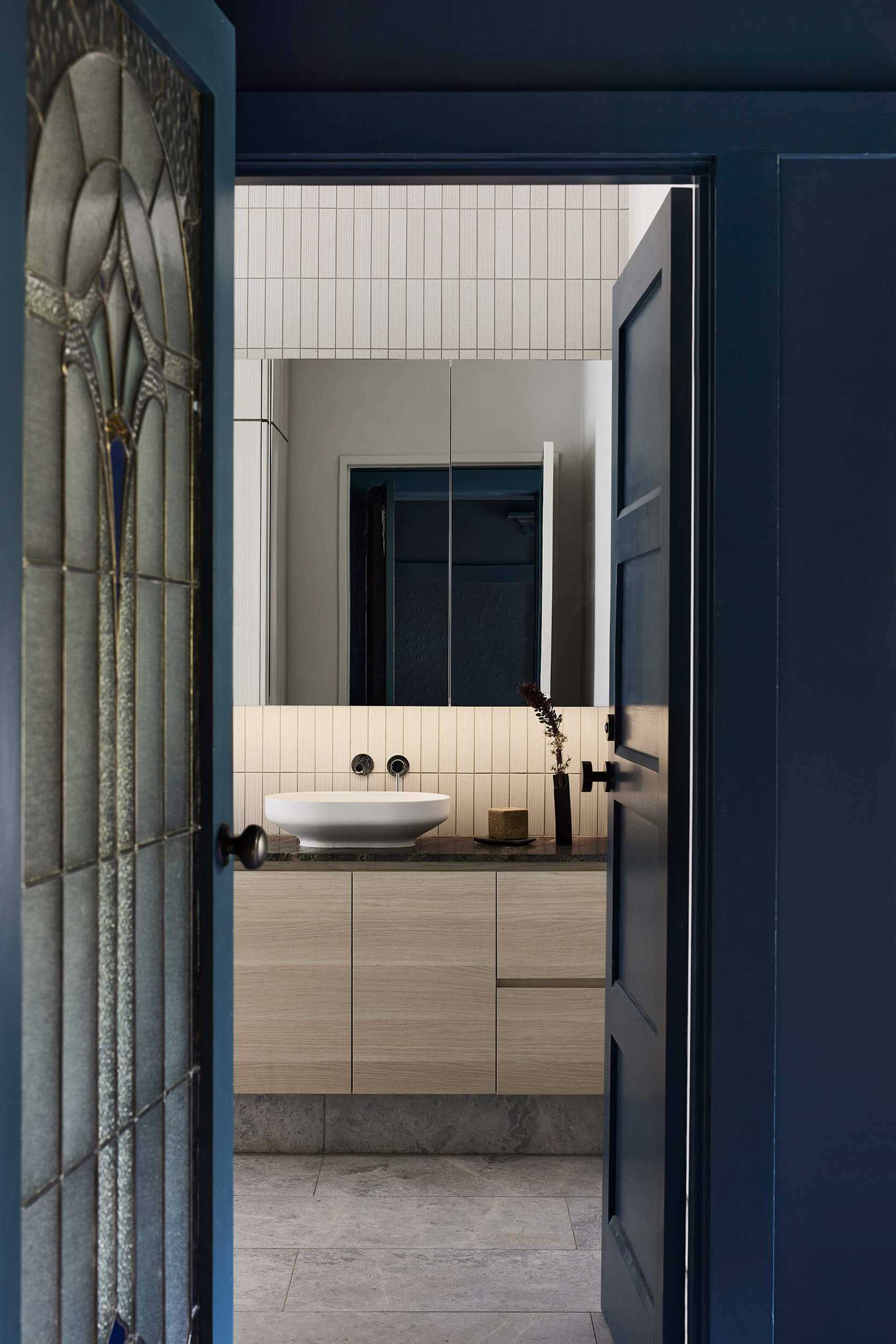 In this bathroom, vertically placed tiles draw the eye upwards to the high ceiling, while a wood vanity adds warmth to the space.