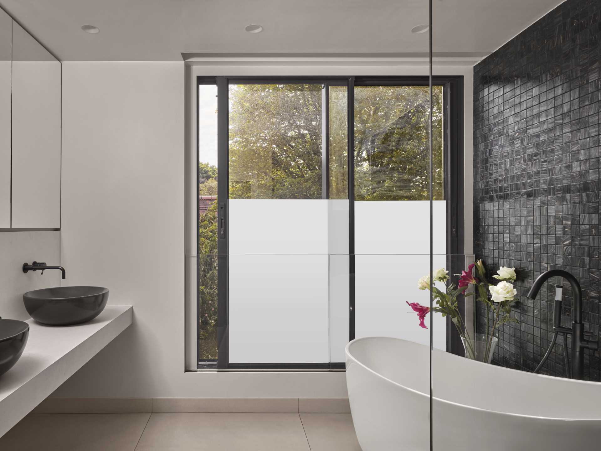 A modern bathroom includes a double vanity, a freestanding bathtub, and a black tile mosaic on the wall.