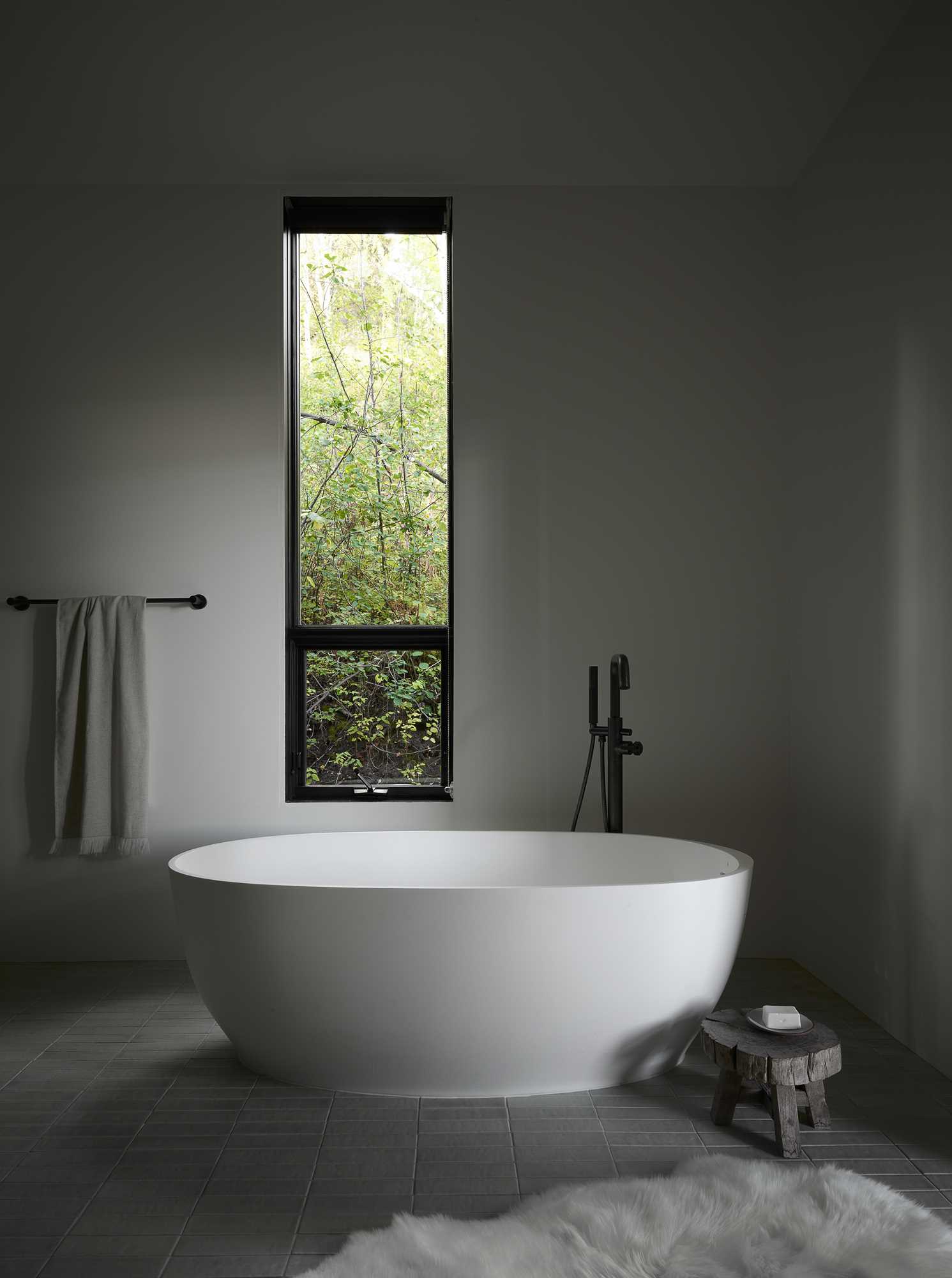 A modern bathroom with a freestanding bathtub and thin vertical window.