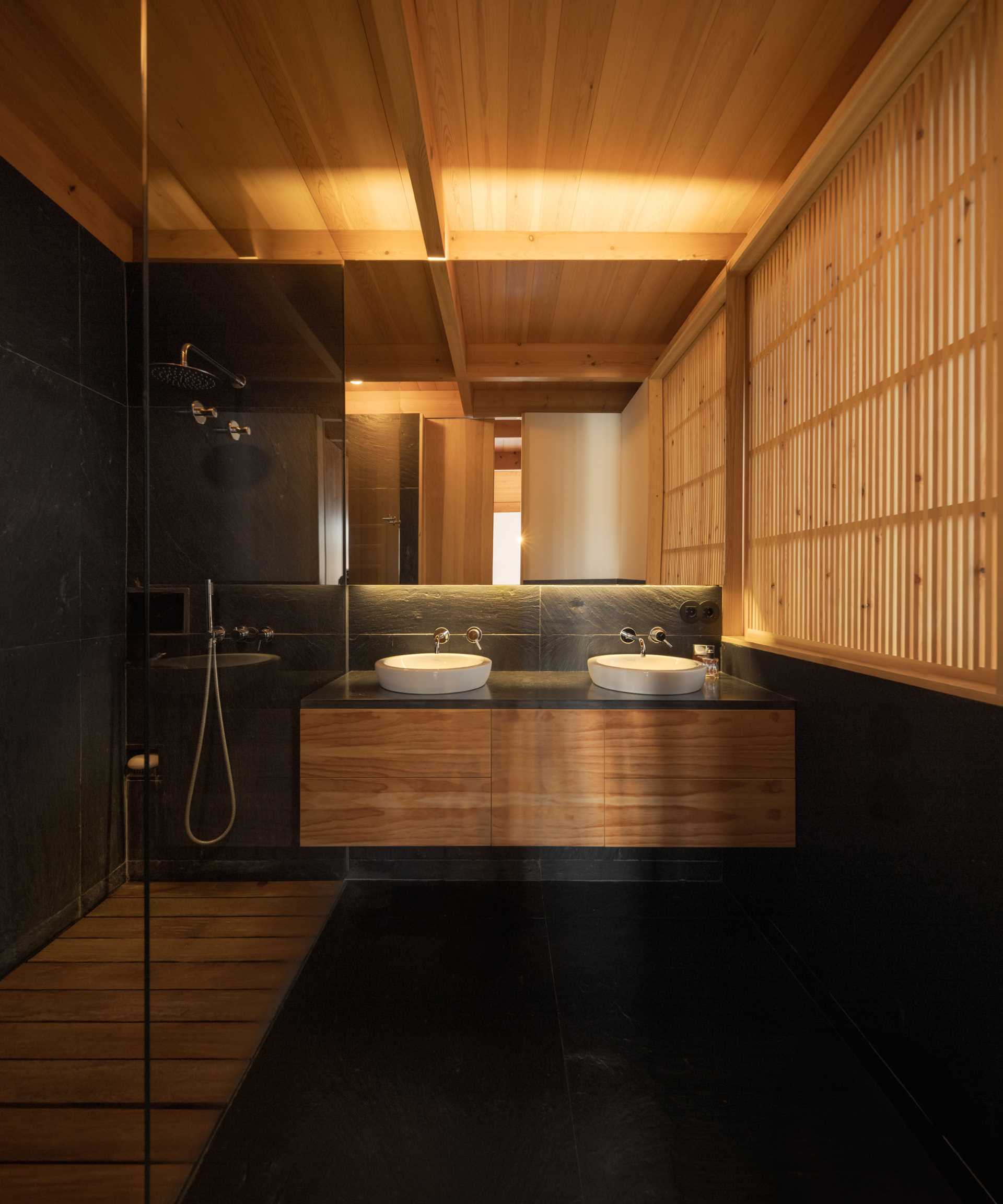 A modern bathroom with wood, dark stone, and hidden lighting.