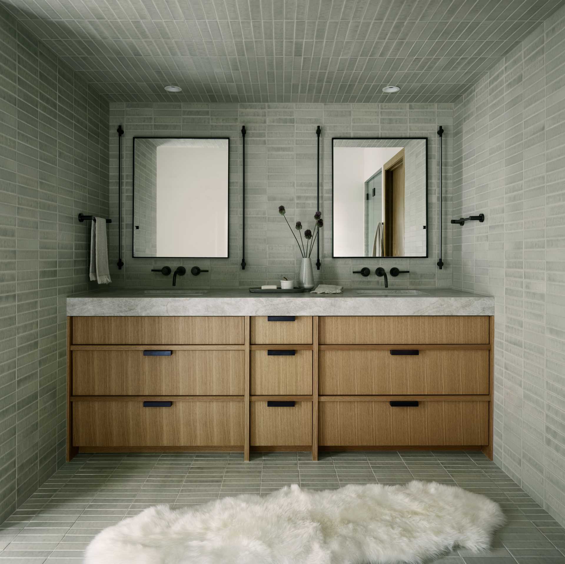 In the en-suite bathroom, tiles cover the walls, floor, and ceiling, while a double wood vanity adds a natural element to the ،e.