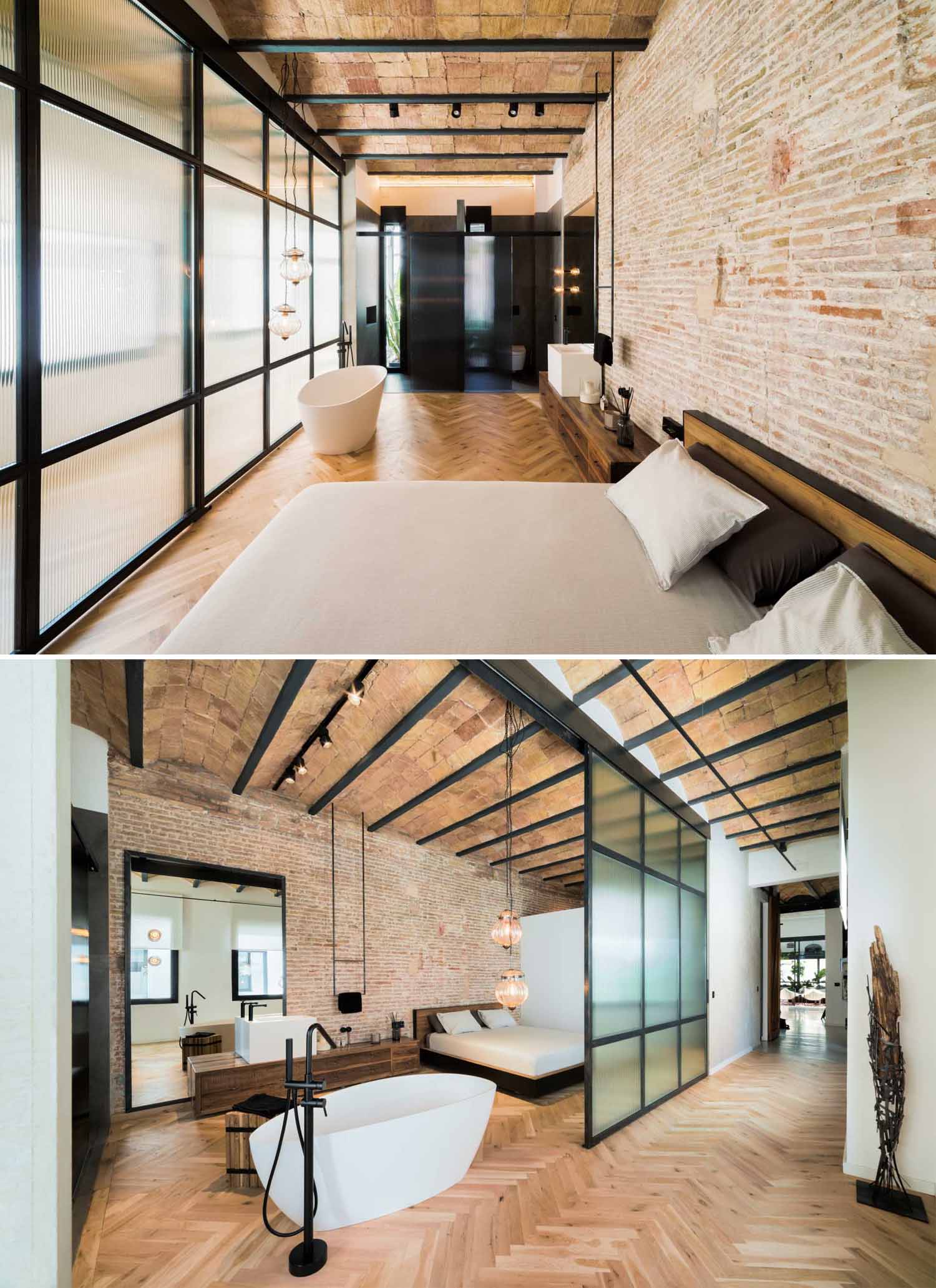 In this primary bedroom, herringbone flooring spans both the sleeping area and the bathroom, with a freestanding bathtub positioned in front of a large sliding glass door.