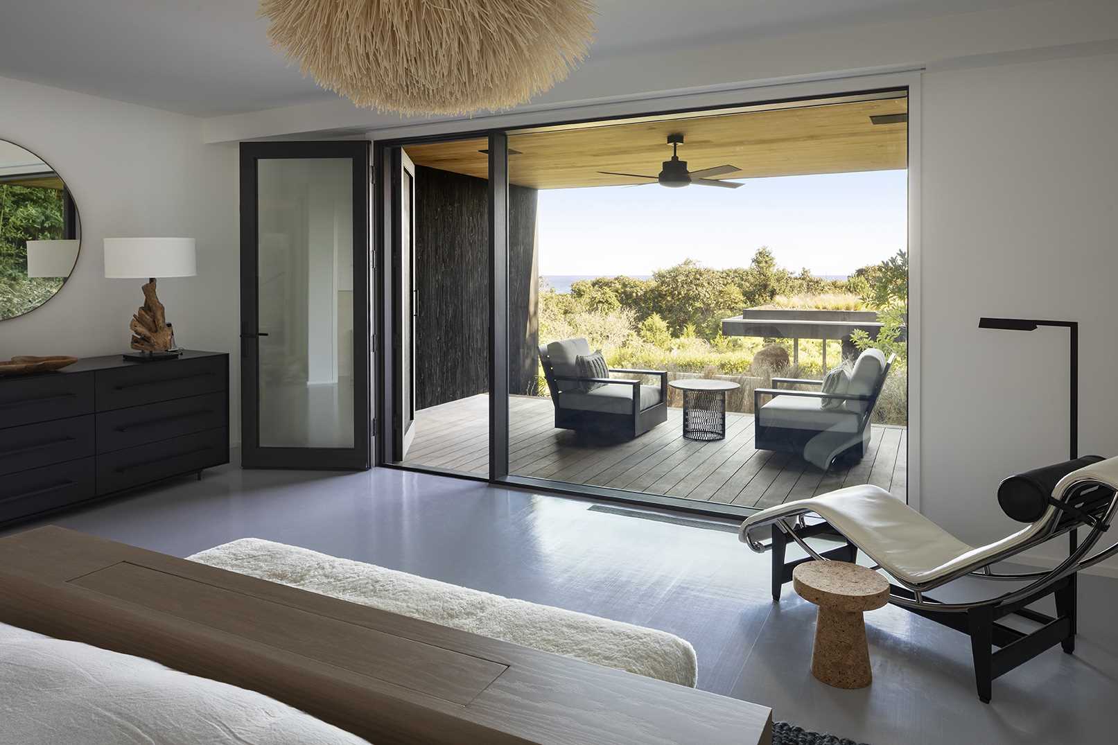 A modern bedroom with a private outdoor space that has views of the garden and water in the distance.