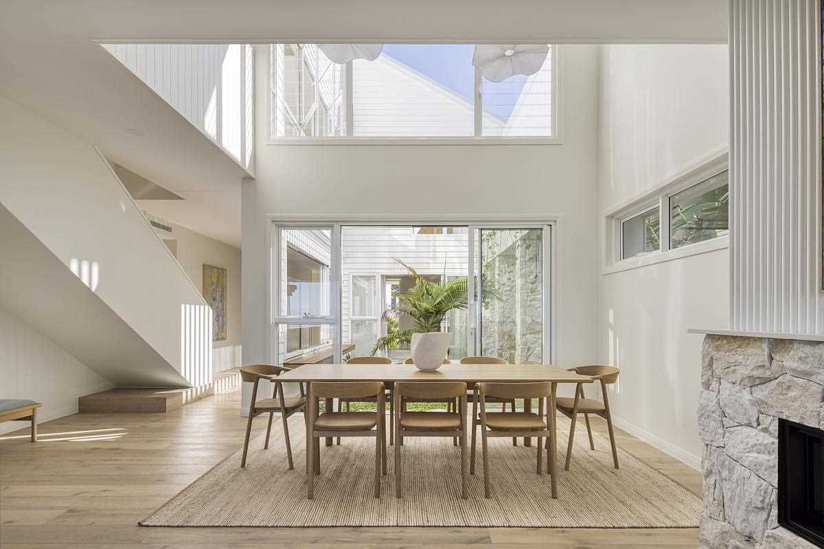 This modern coastal-inspired dining area includes a double-height ceiling and an abundance of natural light.