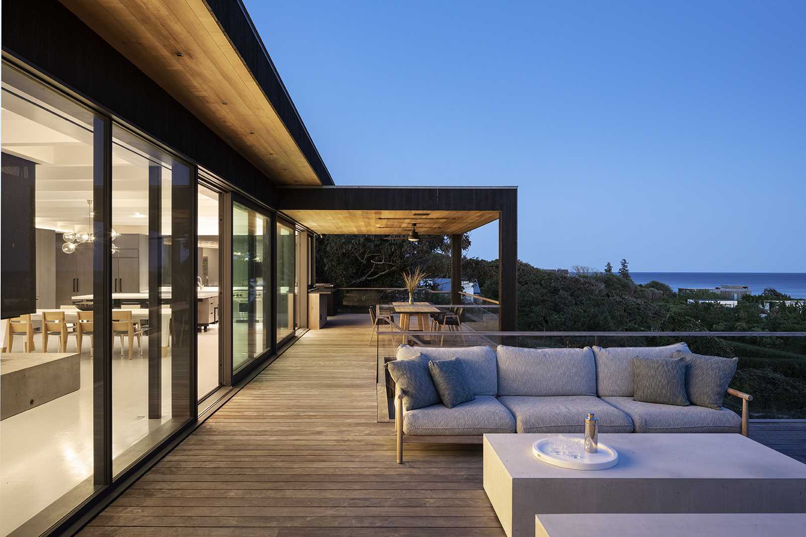 A modern kitchen with a large island opens to a covered deck with outdoor dining and a lounge.