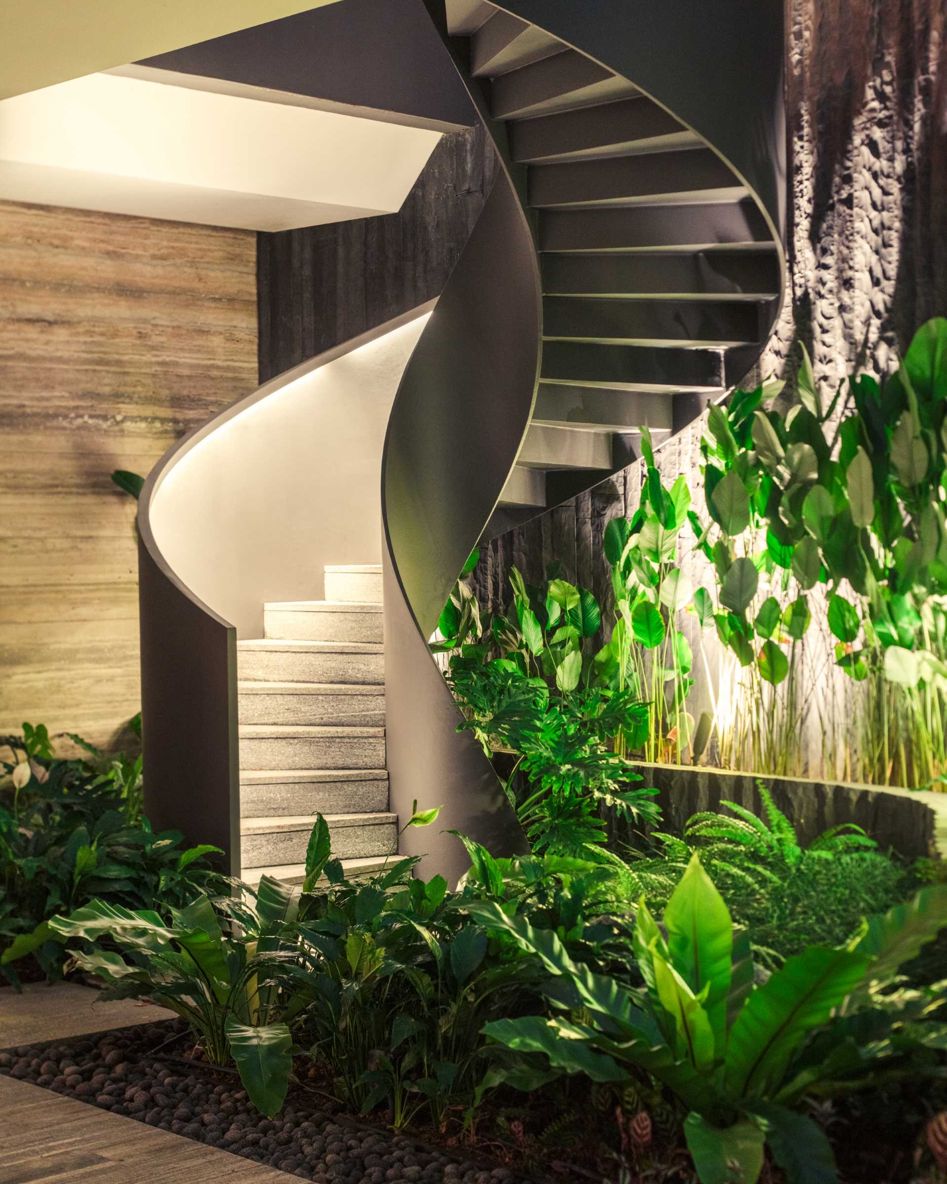 A modern home with external spiral stairs that's surrounded by plants.