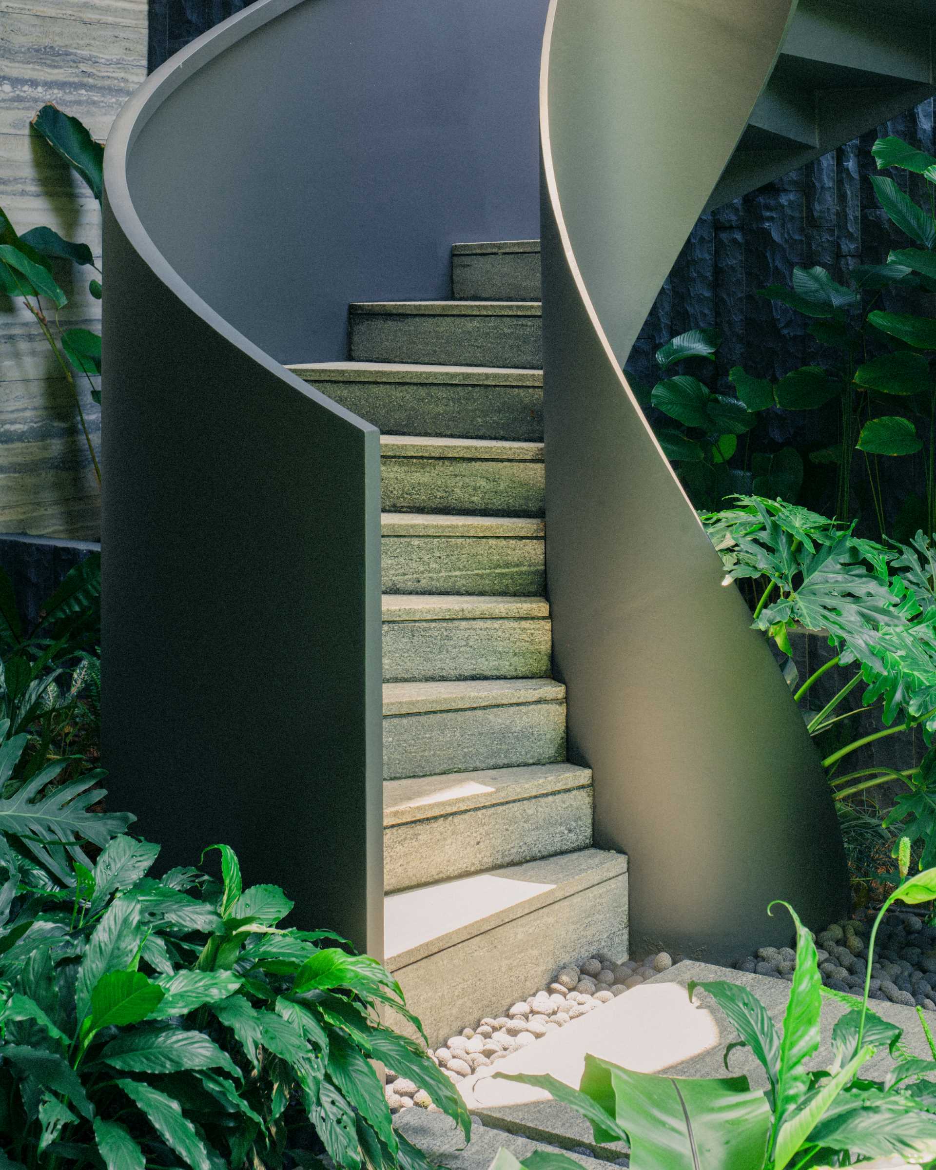 A modern home with external spiral stairs that's surrounded by plants.