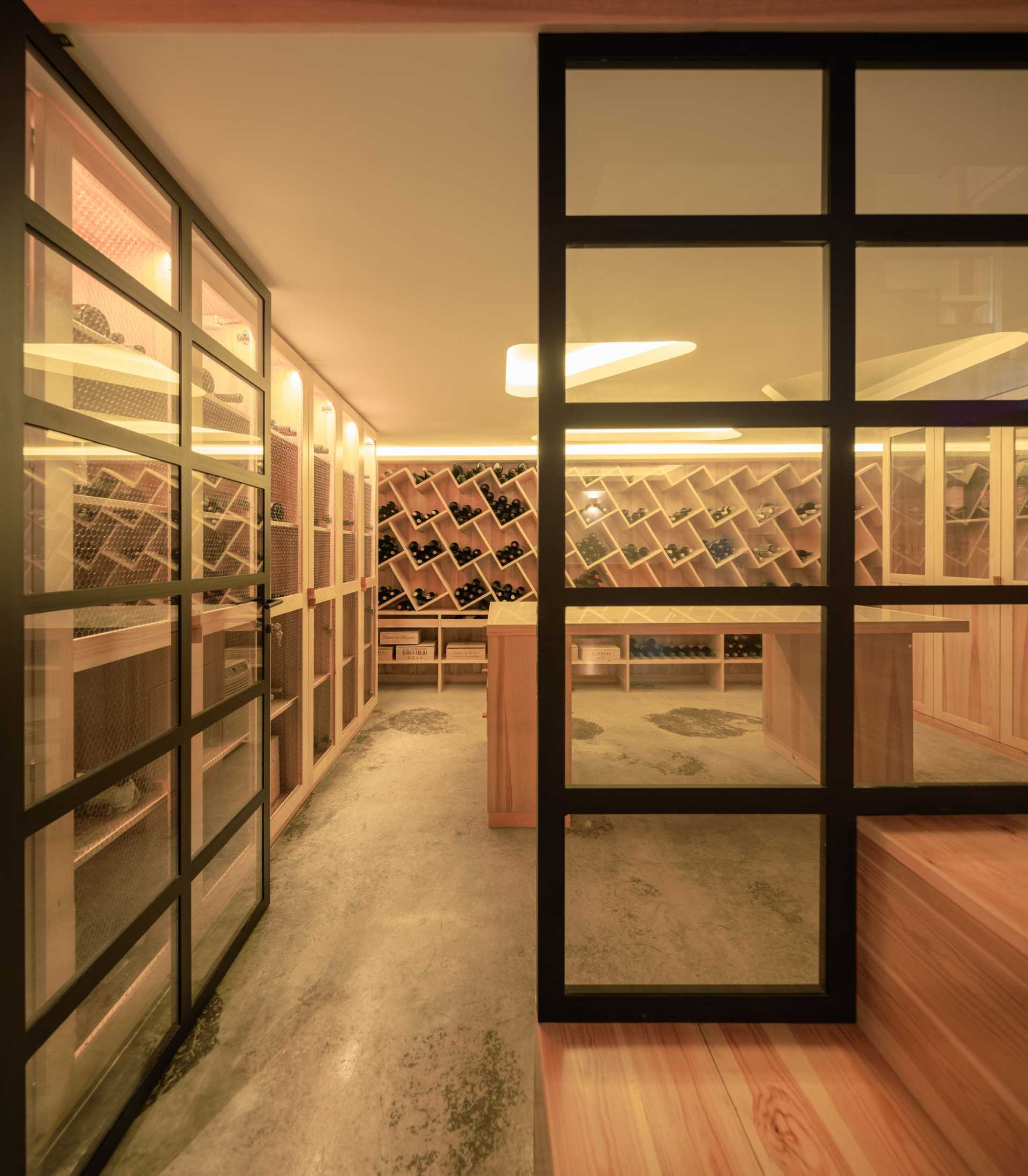 A modern wine cellar with built-in shelving, a central table, and glass doors.