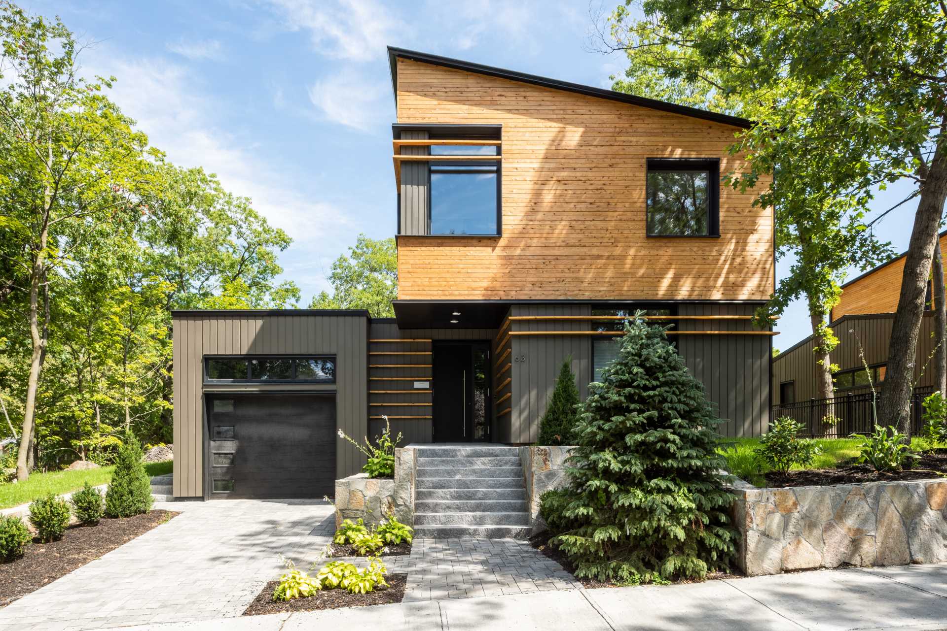 A modern home features an angled roof line, a clear-finished white cedar siding on the upper volume, and a painted siding made from materials recovered from manufacturing by-products on the lower volume.