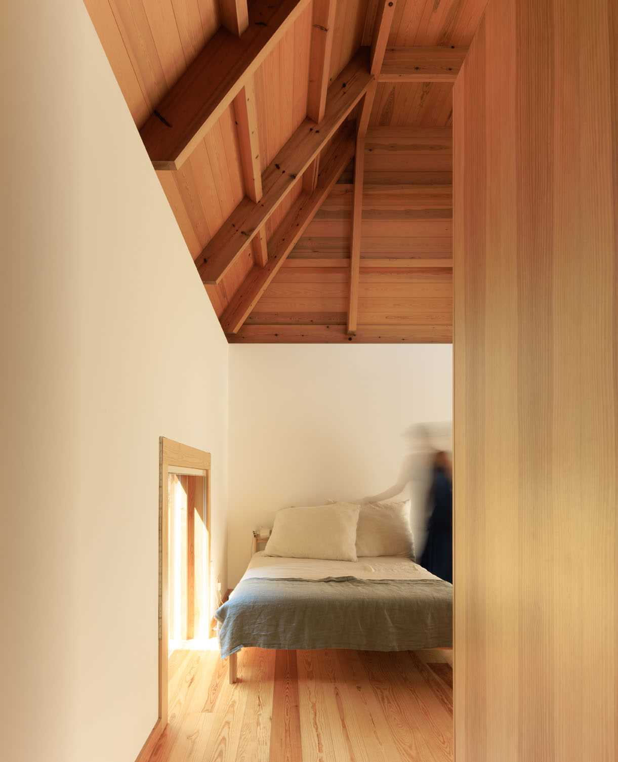 A modern and minimalist bedroom with a low window and high wood ceiling.