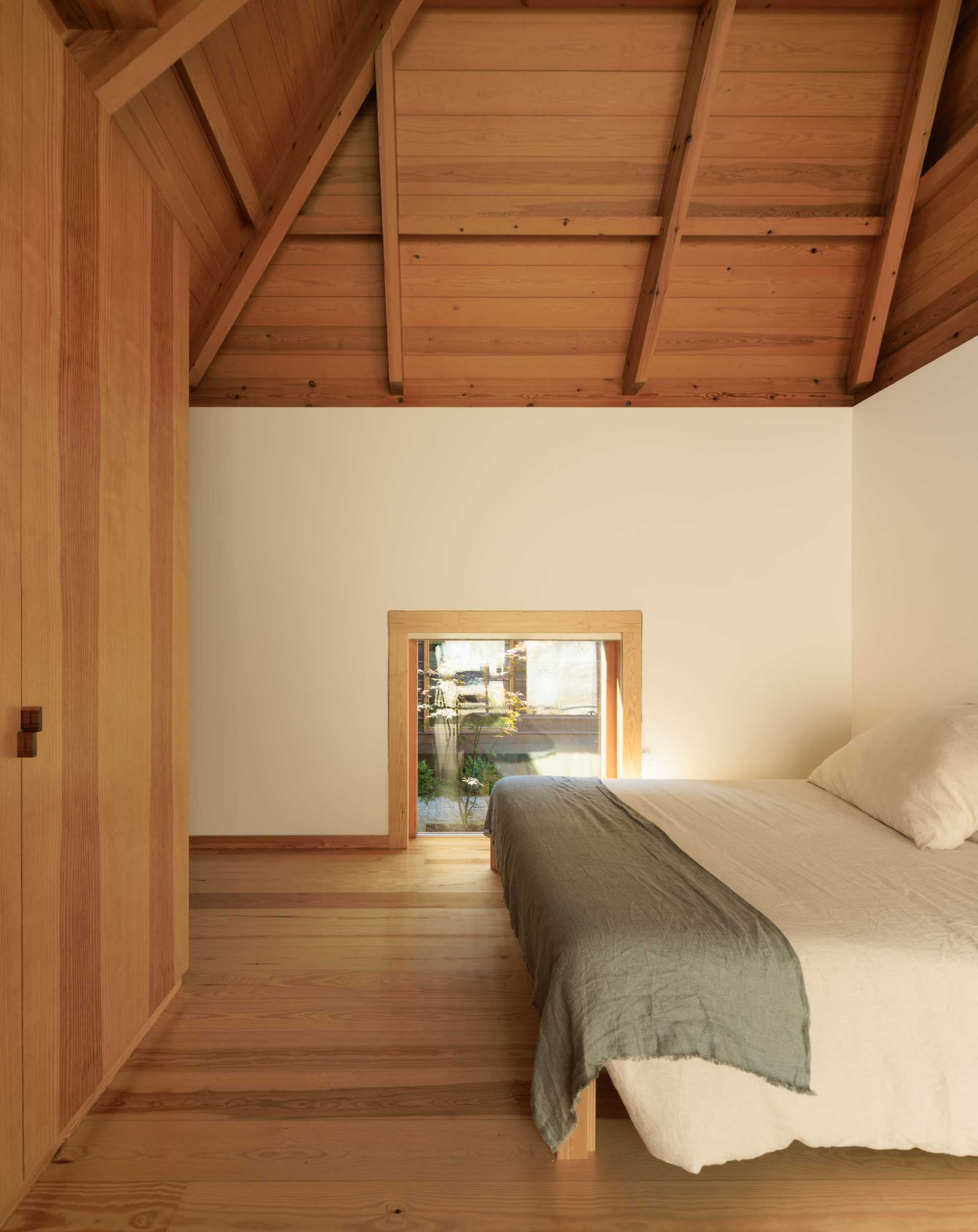 A modern and minimalist bedroom with a low window and high wood ceiling.