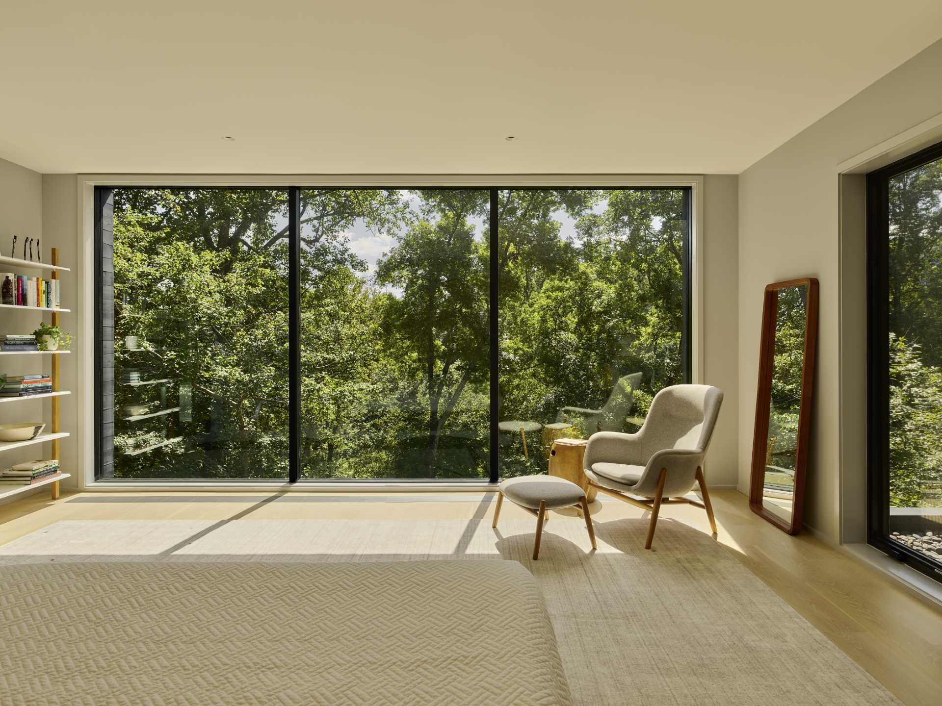 In this modern bedroom, floor to ceiling windows that provide an abundance of natural light and frame the tree views.