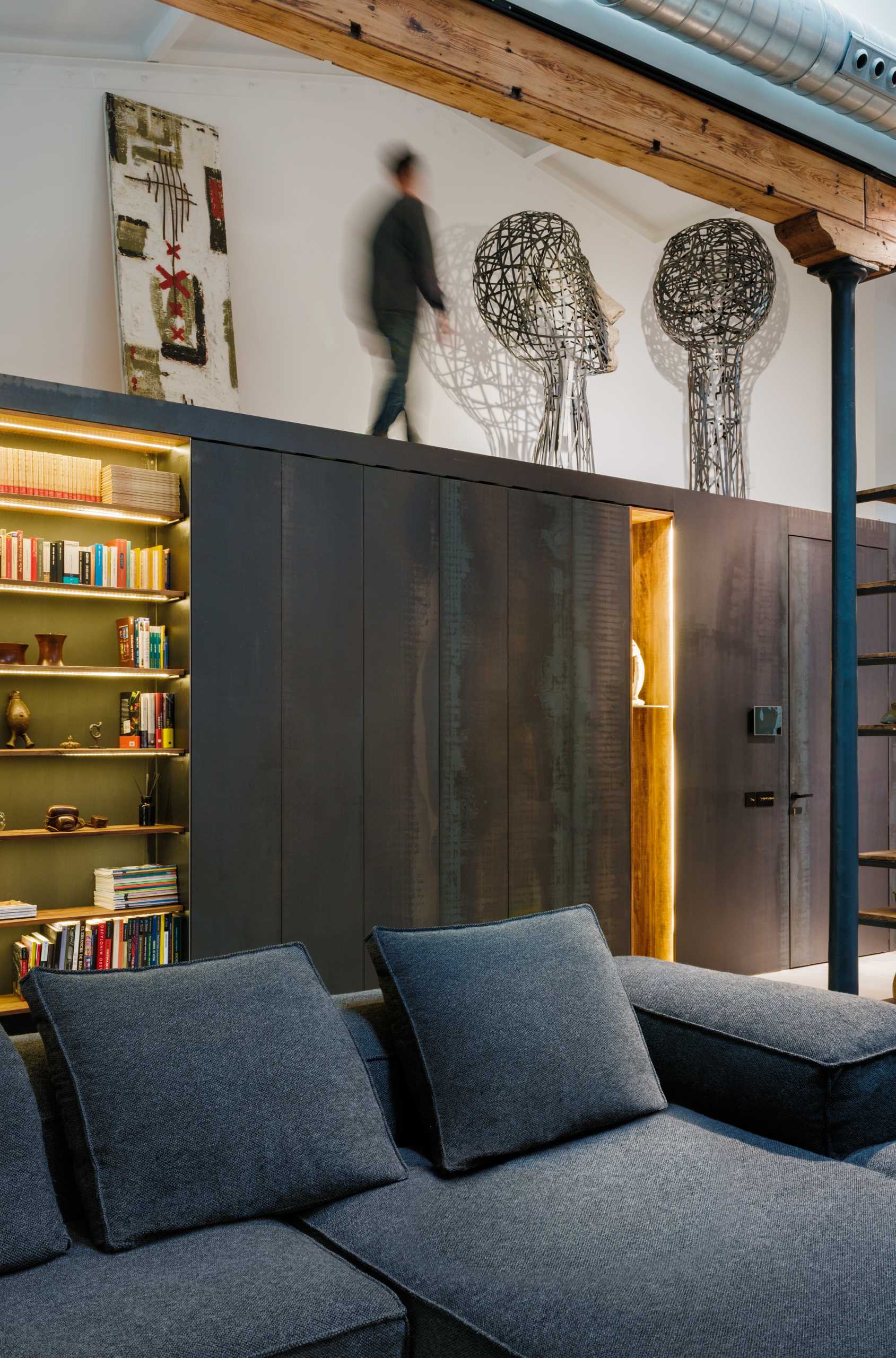 A wall of steel design elements includes shelving with hidden lighting, before transitioning into the kitchen cabinets.