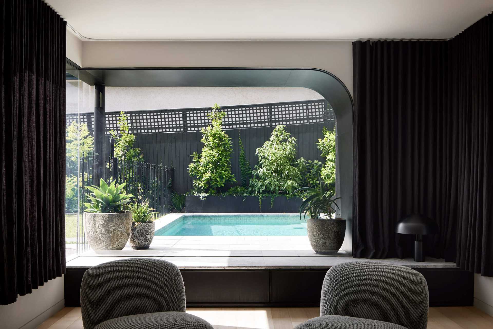 A modern living room with an arched window with views of the pool.