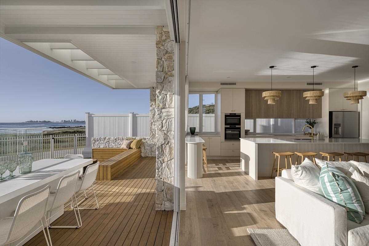A modern coastal home with a designated outdoor space area for sitting, dining, and a swimming pool.