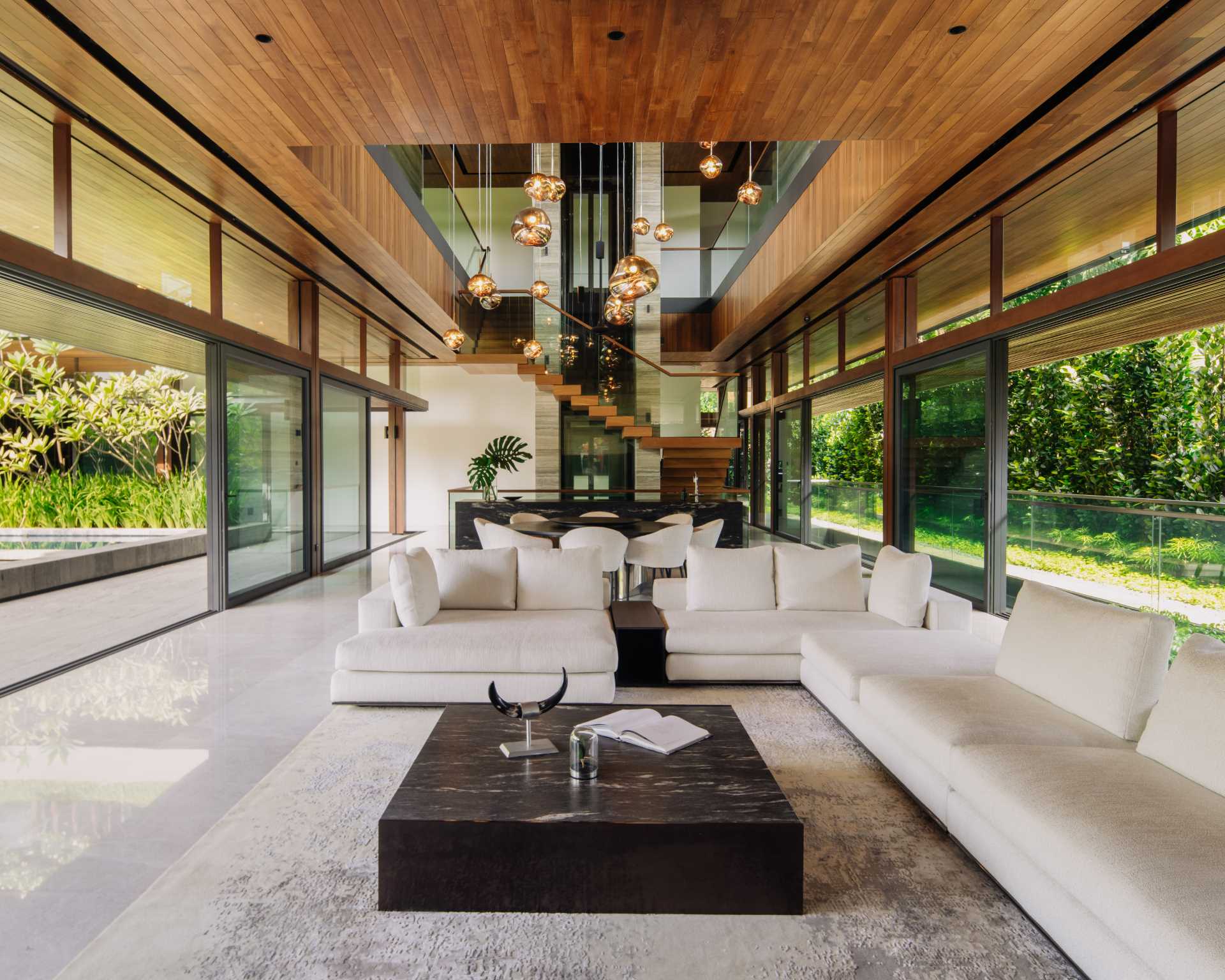 A modern open-plan living room and dining area with high wood ceilings and sliding glass doors that connect with the outdoor spaces.