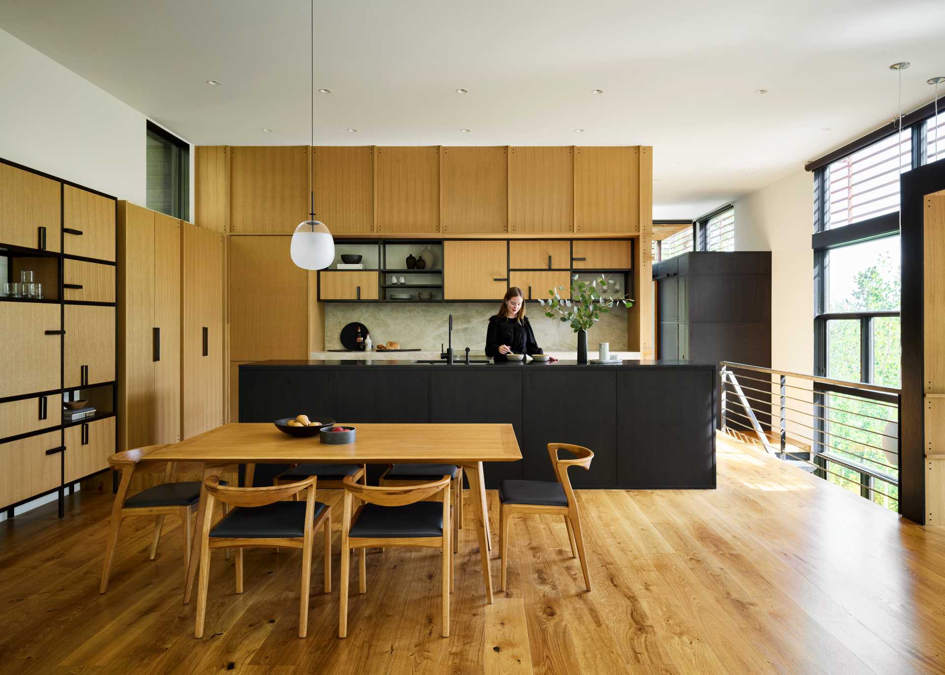 A modern open-plan dining area and kitchen with white oak cabinets and black accents.