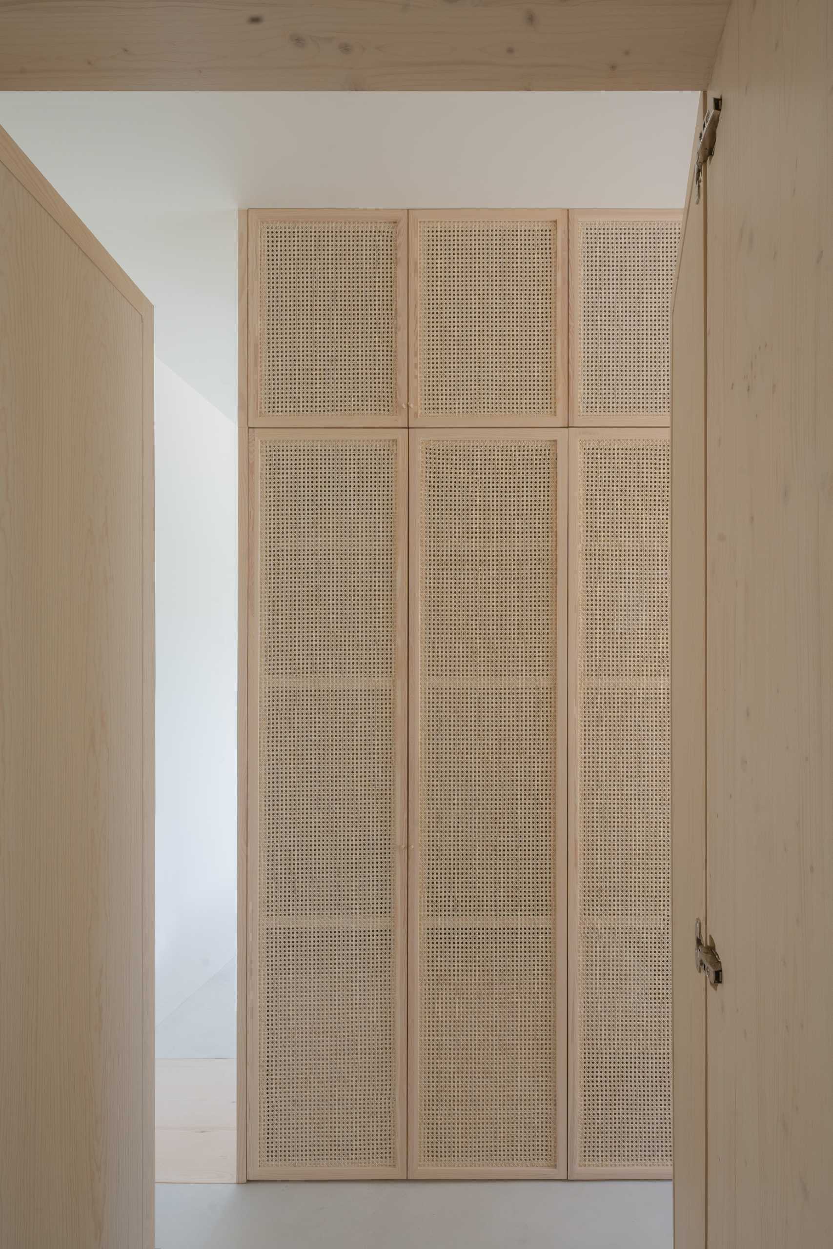 A walk-in closet with artisanal rattan and light pine wood carpentry.