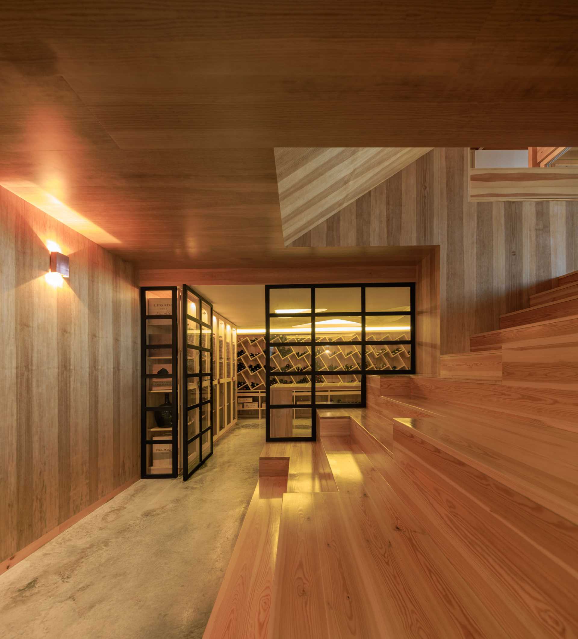 A modern wine cellar with built-in shelving, a central table, and glass doors.