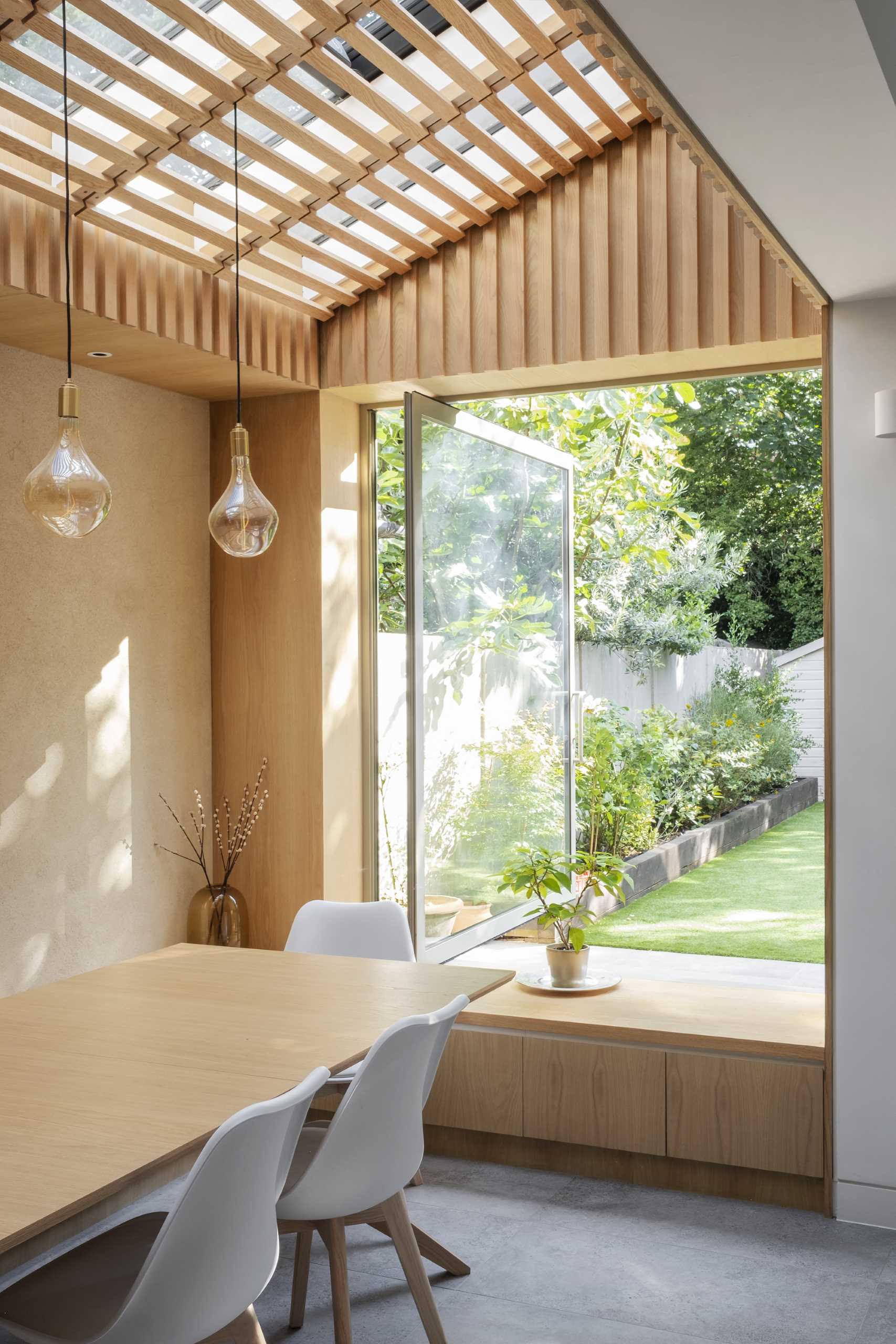 A large pivoting window connects a dining room to the garden.