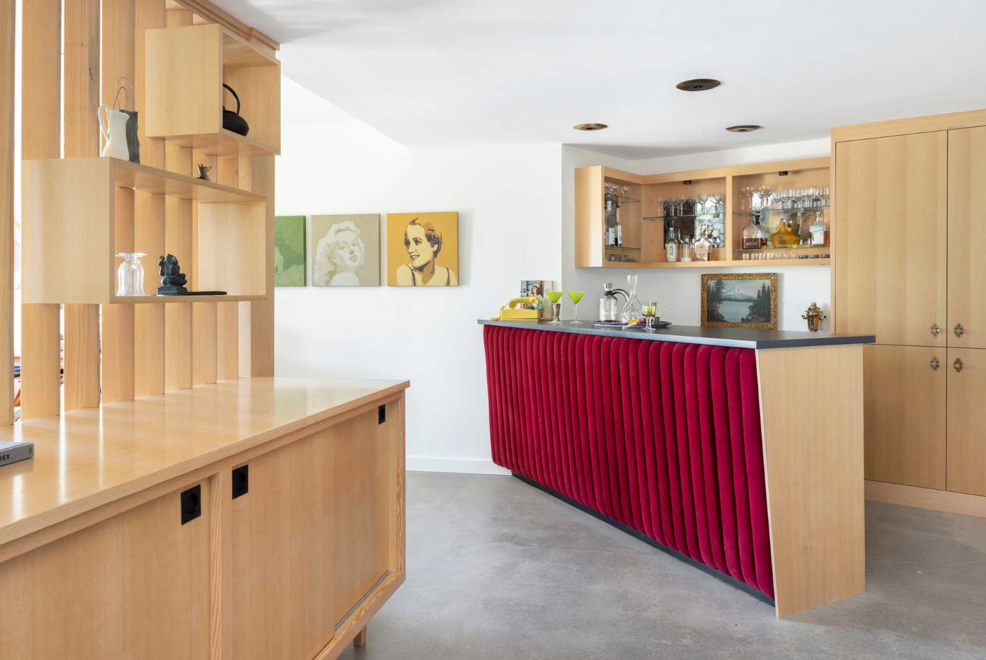 An original mid-century modern built-in bar received a fresh facade with a dramatic red velvet channel tuft upholstery, and new dark countertops.