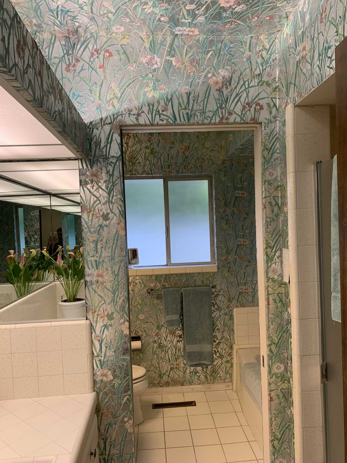 Metallic wallpaper with flowers covered the walls and ceiling in this 'before' bathroom. Also included are vanities that are separated by a wall, both of which have tiled countertops.