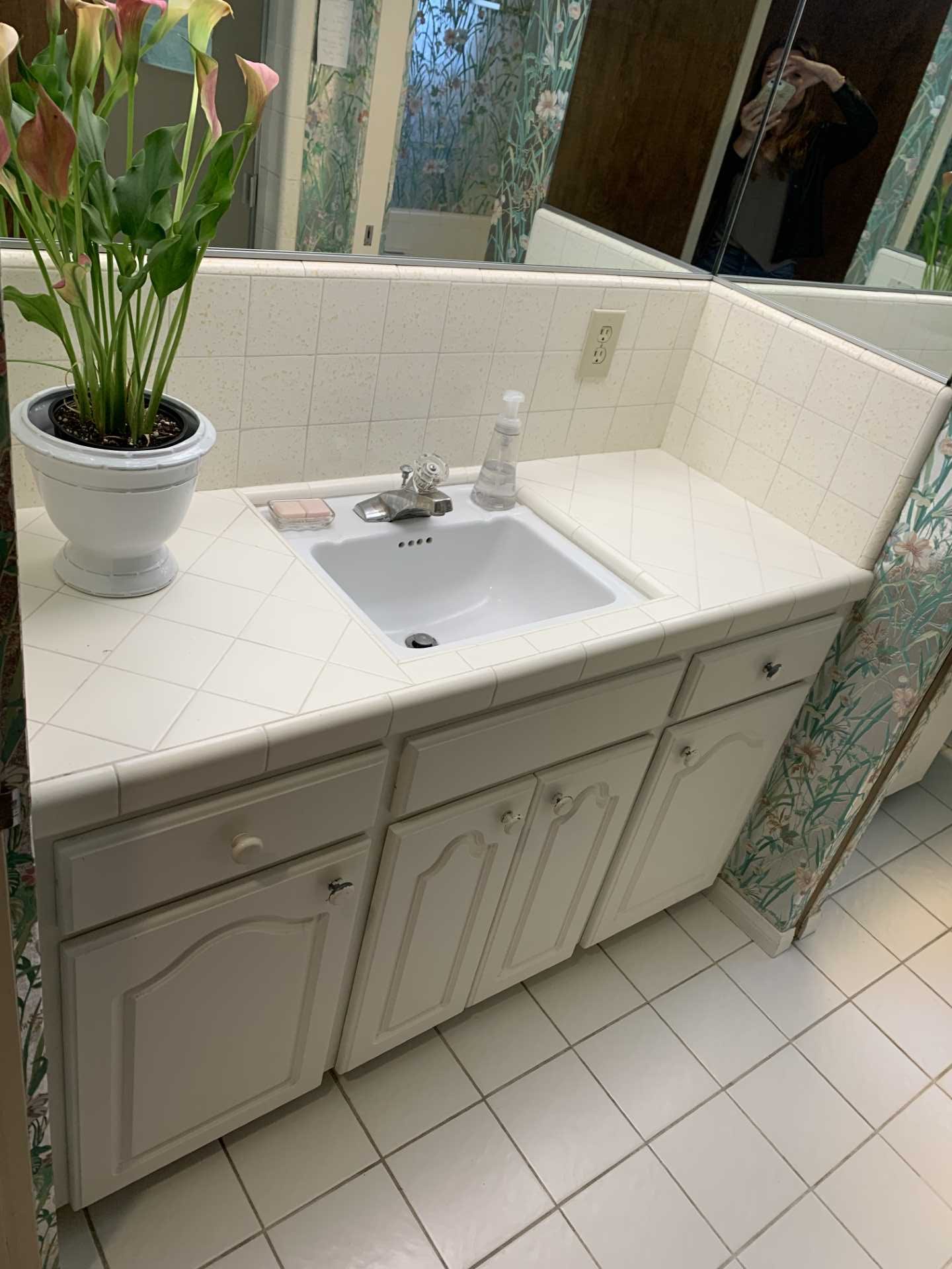 Metallic wallpaper with flowers covered the walls and ceiling in this 'before' bathroom. Also included are vanities that are separated by a wall, both of which have tiled countertops.