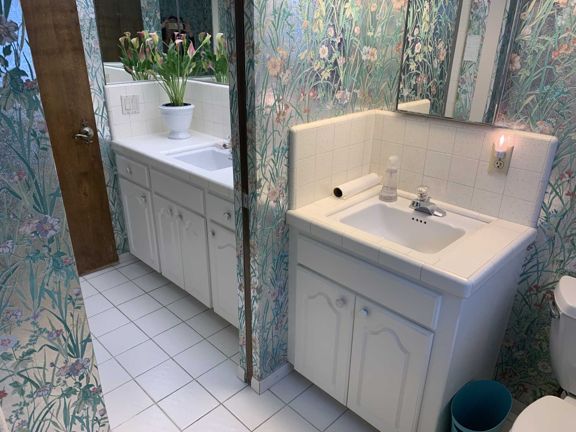 Metallic wallpaper with flowers covered the walls and ceiling in this 'before' bathroom. Also included are vanities that are separated by a wall, both of which have tiled countertops.