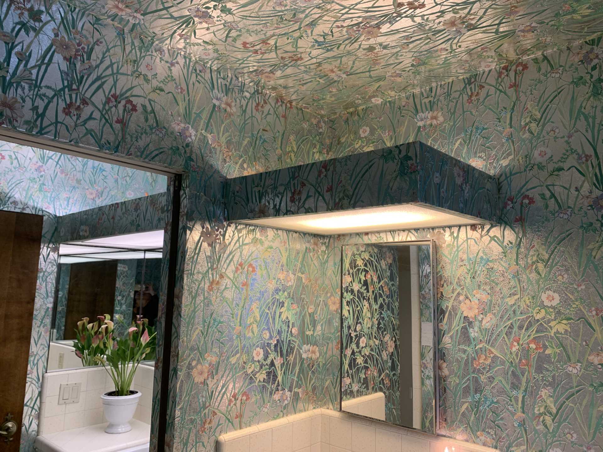 Metallic wallpaper with flowers covered the walls and ceiling in this 'before' bathroom. Also included are vanities that are separated by a wall, both of which have tiled countertops.