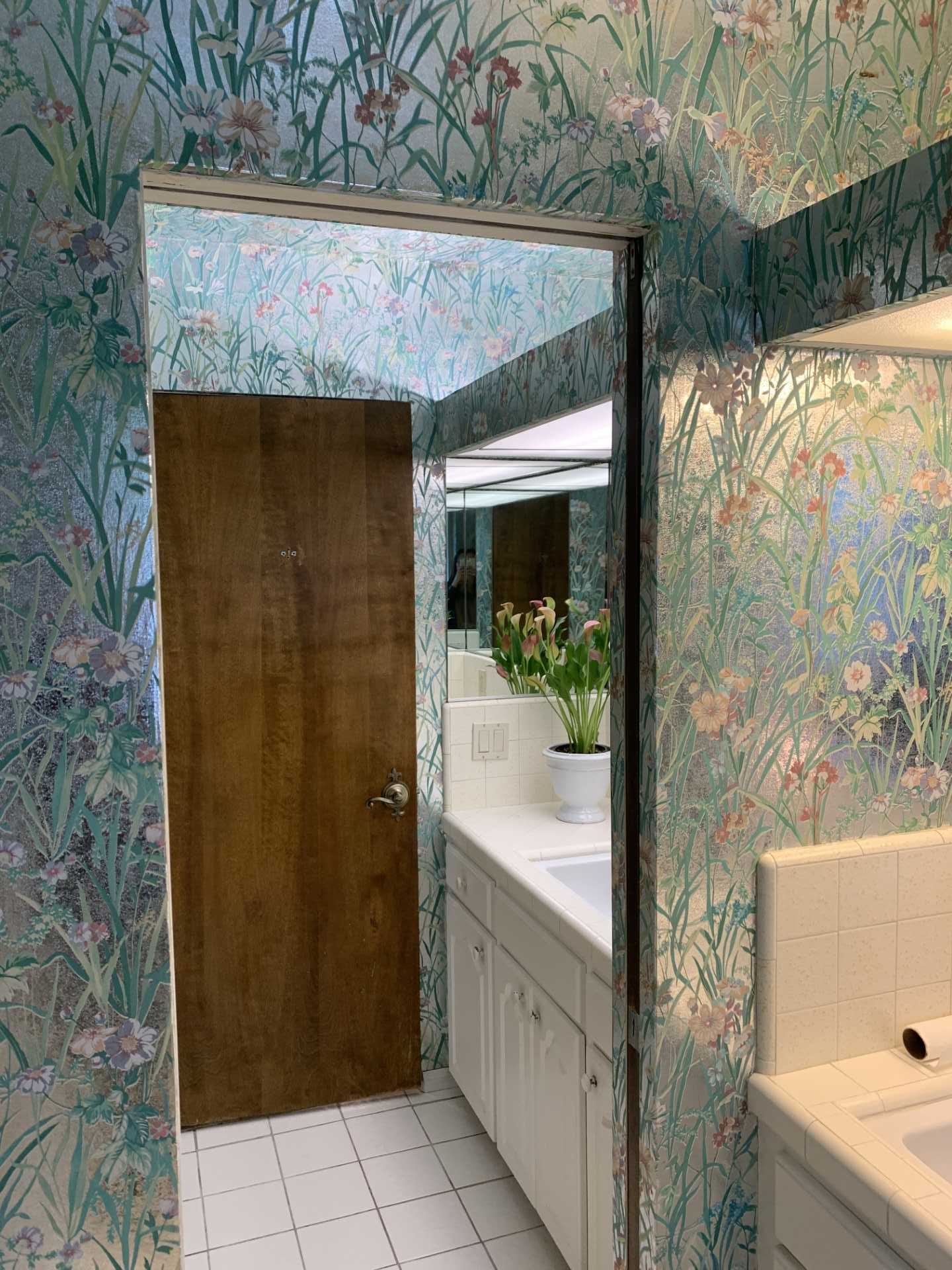 Metallic wallpaper with flowers covered the walls and ceiling in this 'before' bathroom. Also included are vanities that are separated by a wall, both of which have tiled countertops.