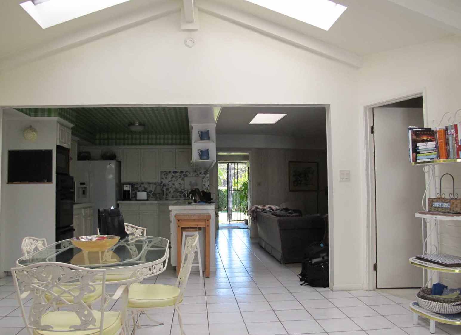 Before - The original kitchen had a tiled floor and countertops, with white cabinets, mismatched appliances, a green tartan wallpapered ceiling, and a floral wallpaper backsplash.