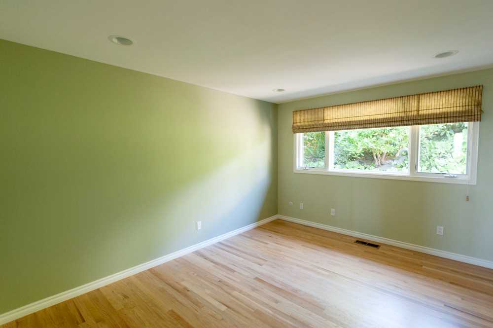 BEFORE - A bedroom with green walls, wood floors, and white window frames.