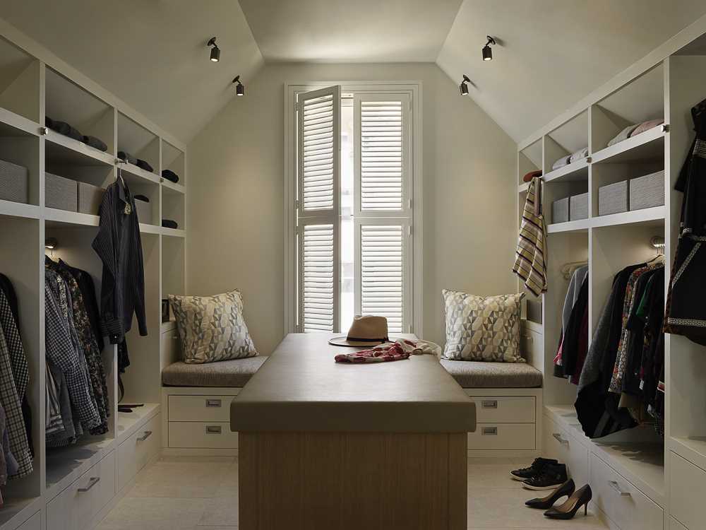 A walk-in closet with built-in shelves on each side and a bench between them.