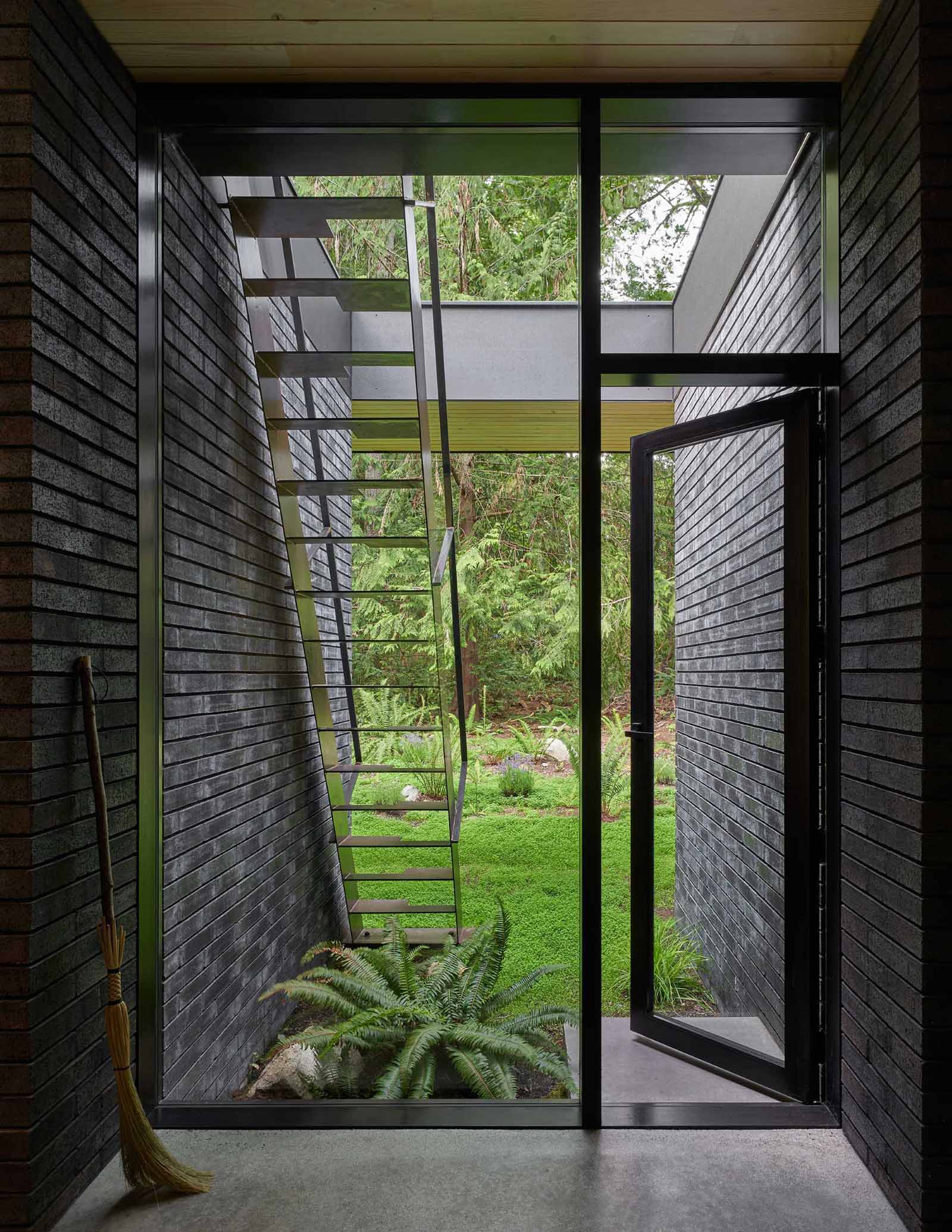 A modern home with a glass door that connects the entryway to the garden and stairs leading to the roof.