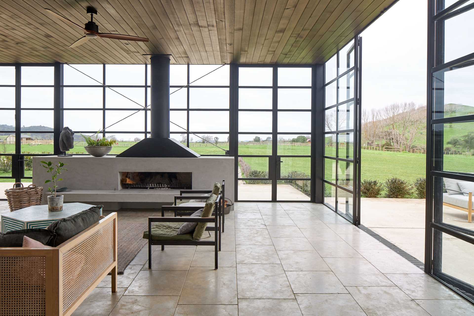 A modern farmhouse has a room with black-framed glass walls that includes a fireplace and living room.