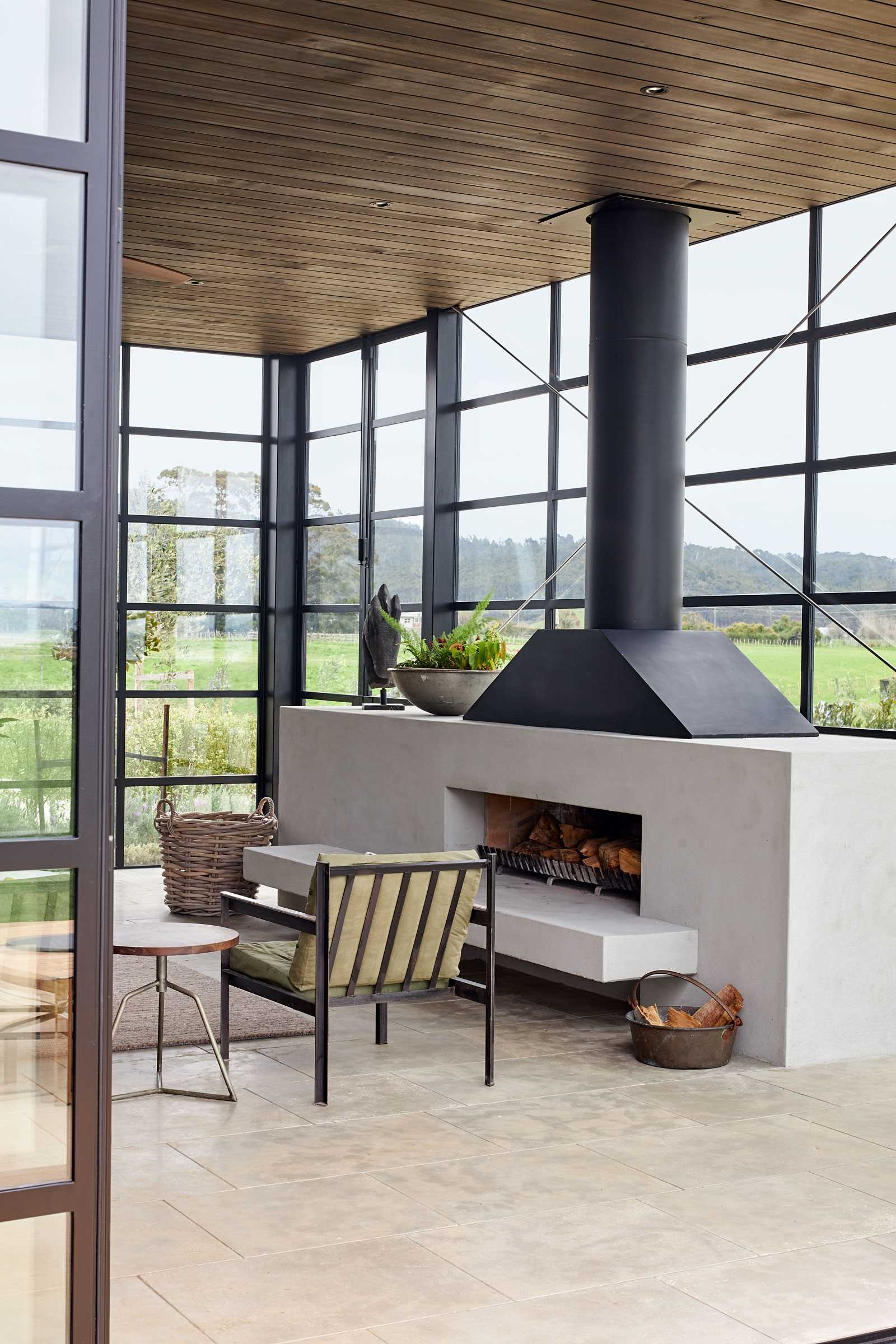 A modern farmhouse has a room with black-framed glass walls that includes a fireplace and living room.