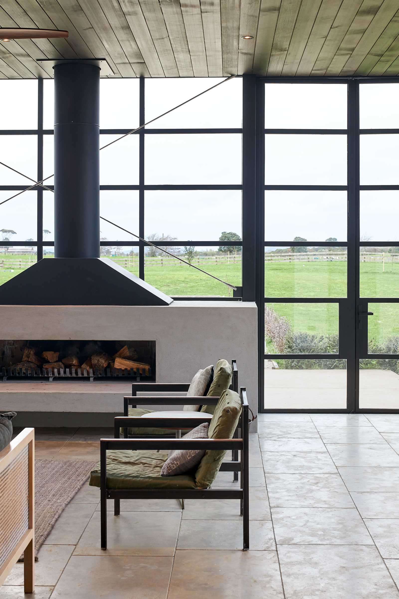 A modern farmhouse has a room with black-framed glass walls that includes a fireplace and living room.