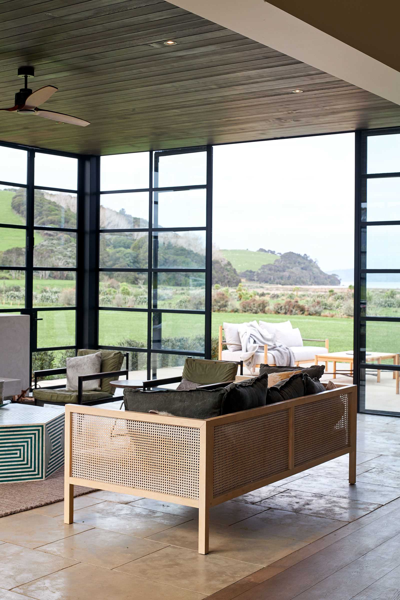 A modern farmhouse has a room with black-framed glass walls that includes a fireplace and living room.