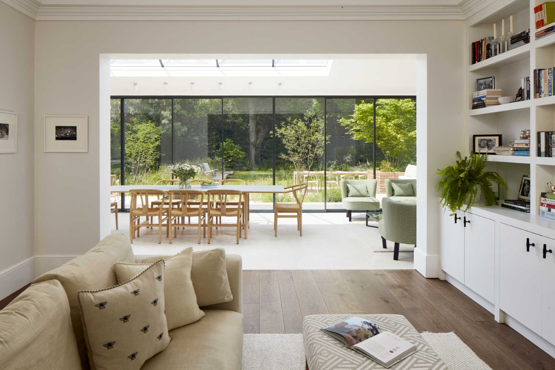 A casual living room with built-in cabinets and shelving, has a view of the light-filled addition and the garden beyond.